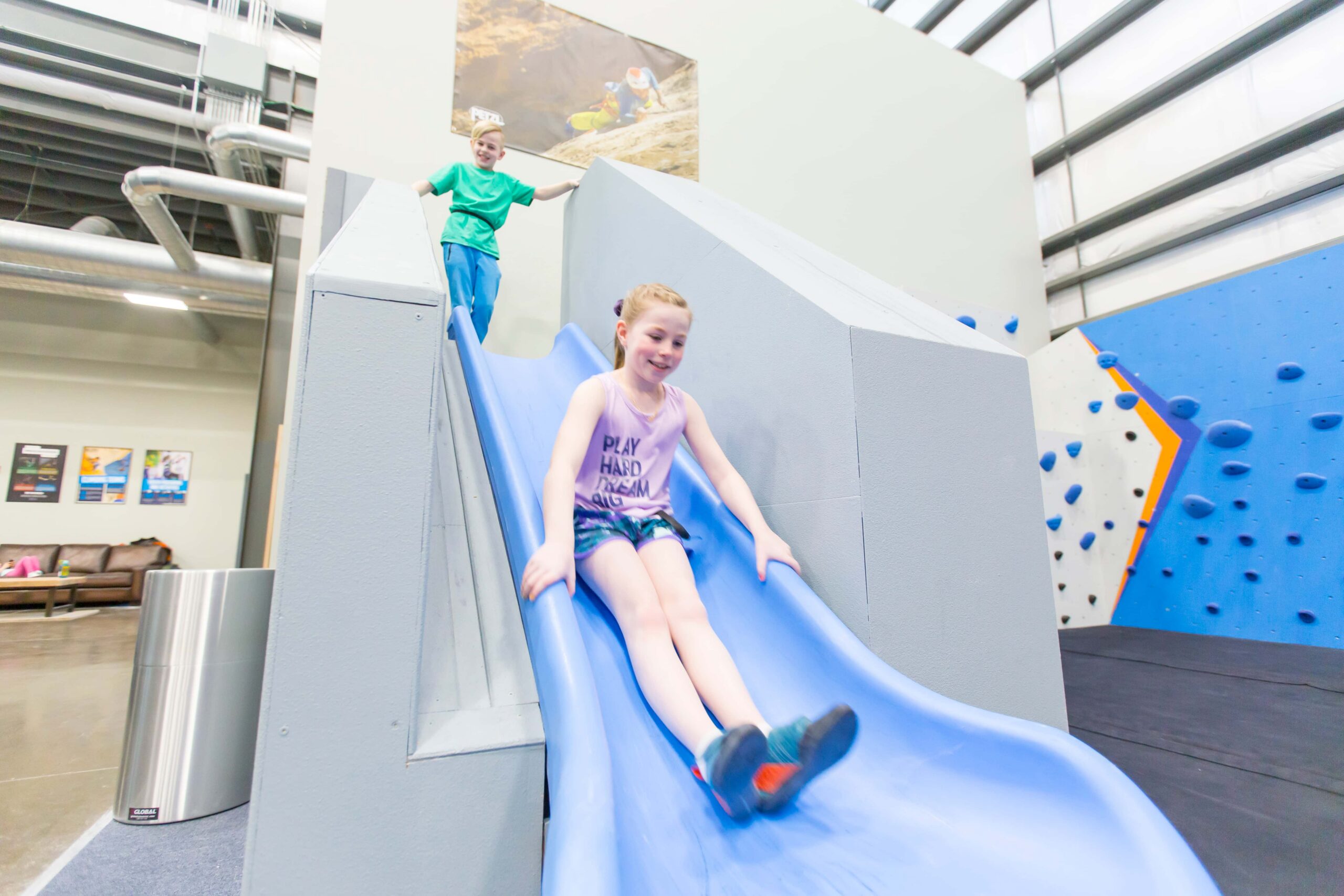 Two kids, a boy and a girl play on a plastic slide in Central Rock Gym Buffalo in the kids area.