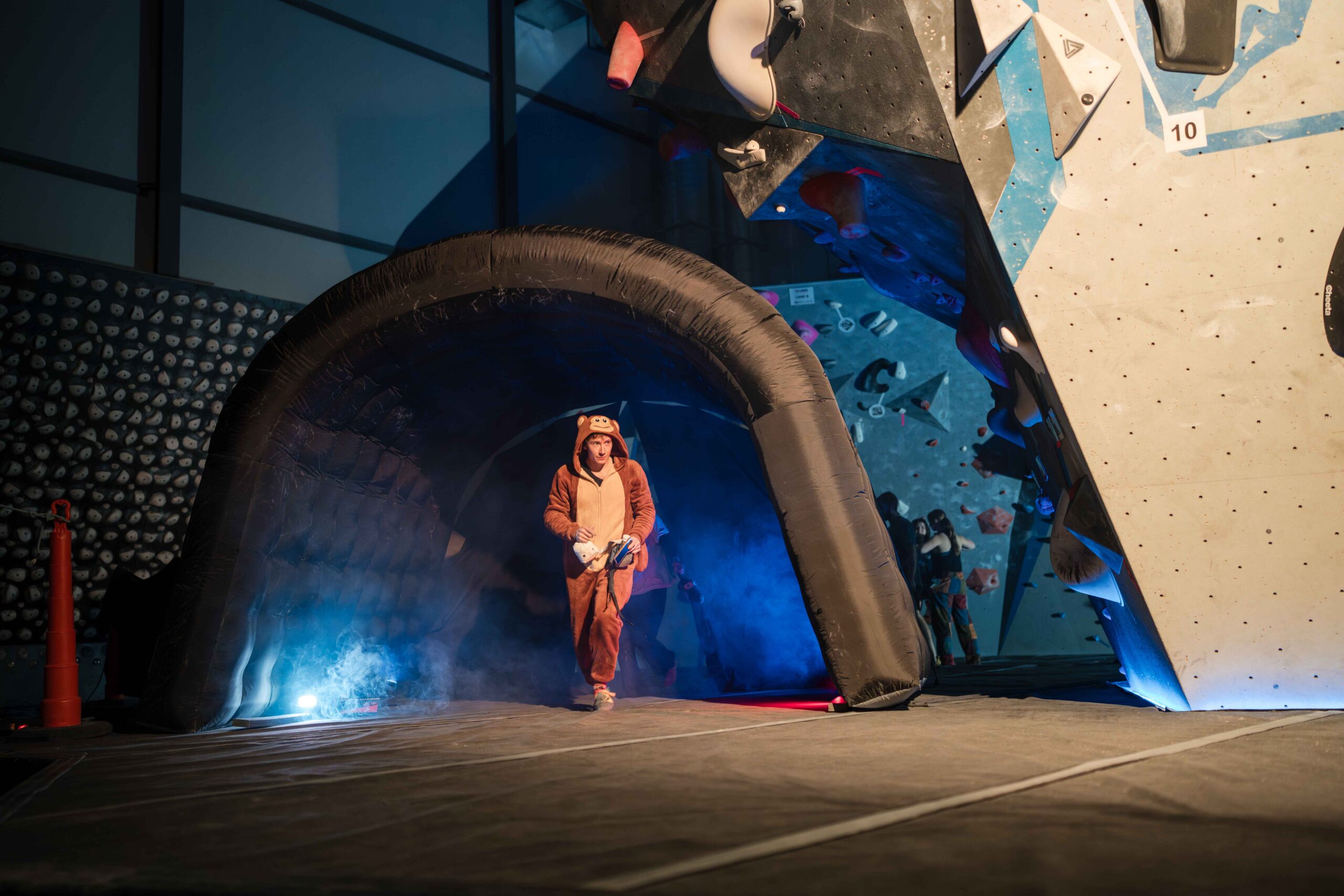 climber wearing a monkey suit walks out of tunnel with cool lights and smoke behind him
