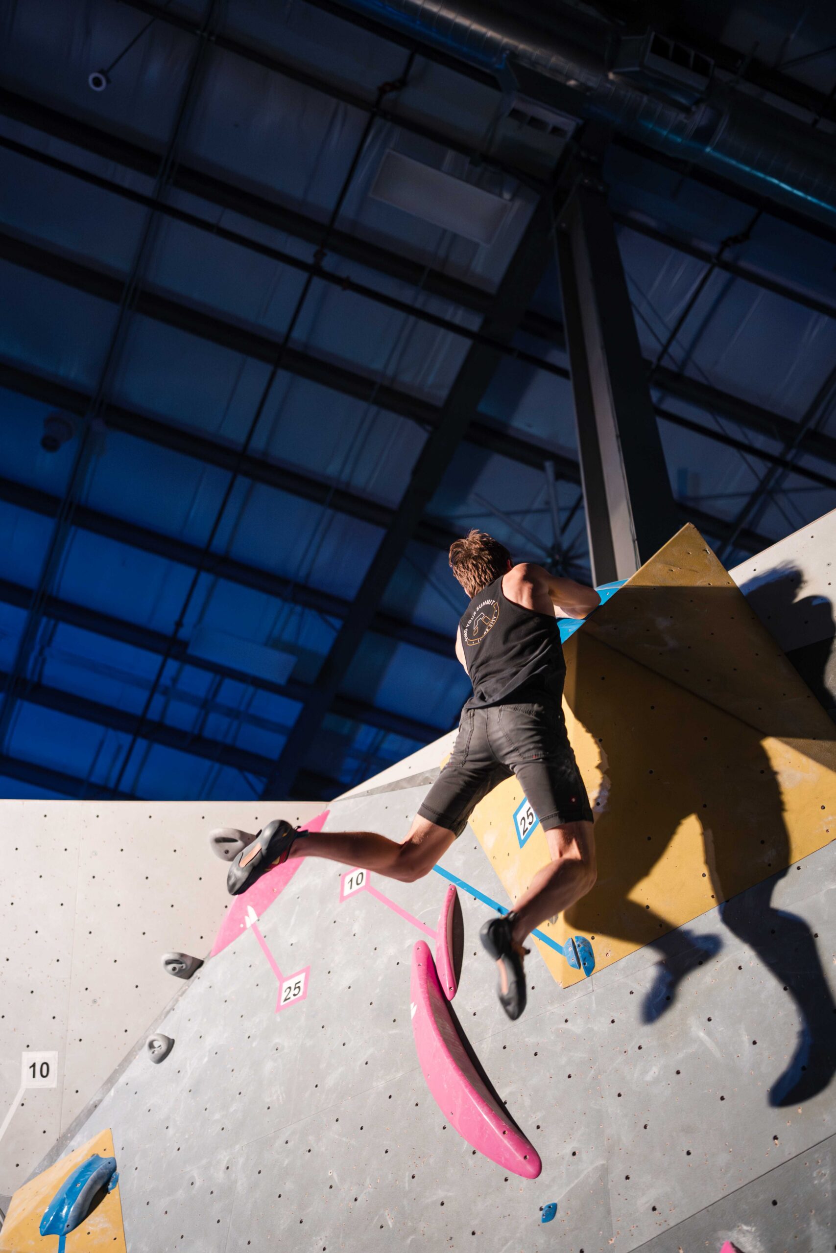 a boulderer's legs swing out as he completes a climb during finals 2025