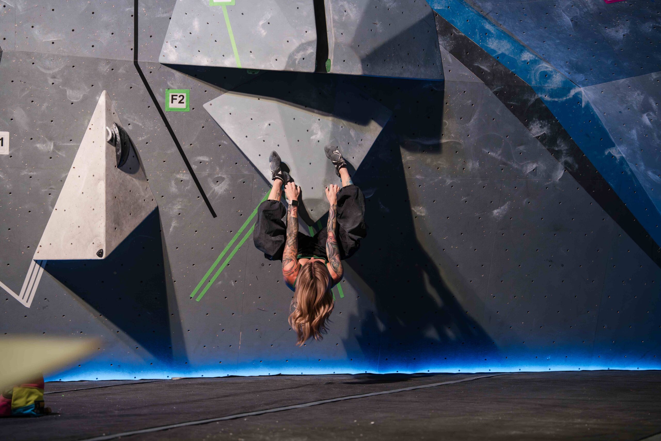 a climber hangs upside down like a bat attempting a finals boulder problem at crg buffalo