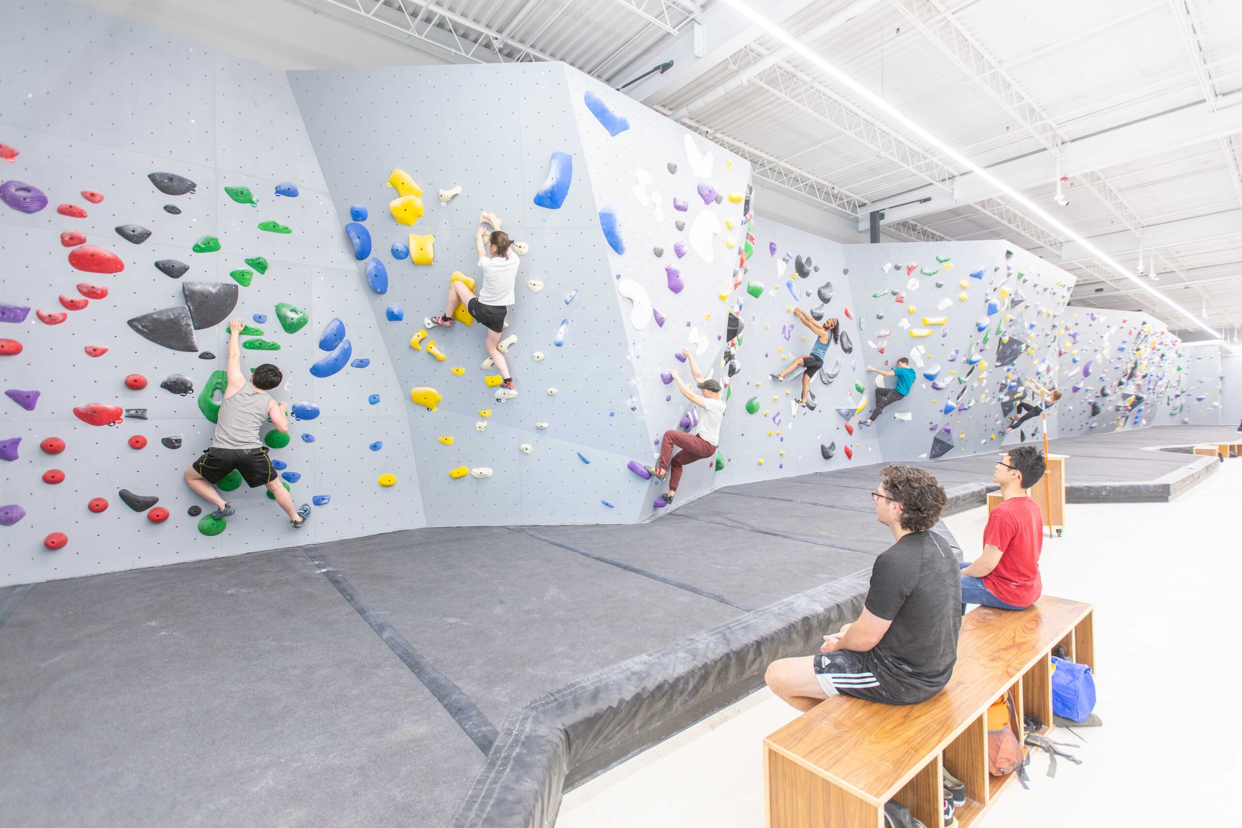 Two men sit on a bench and watch others boulder on the wall at Central Rock Gym Cambridge