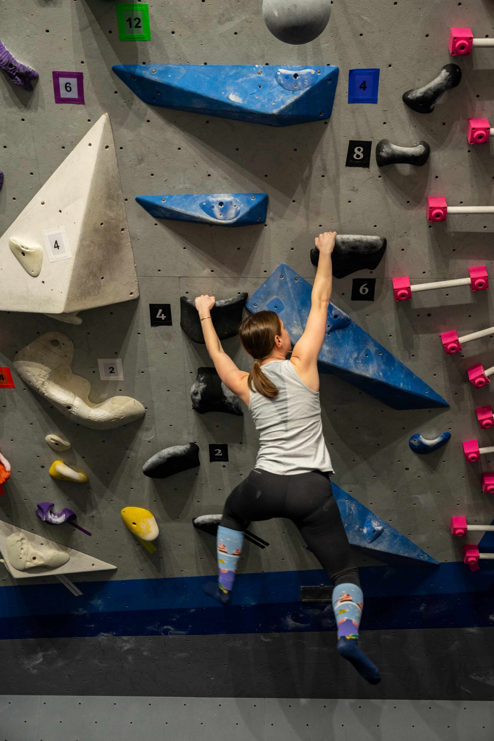 A woman wearing silly socks campuses a bouldering wall.