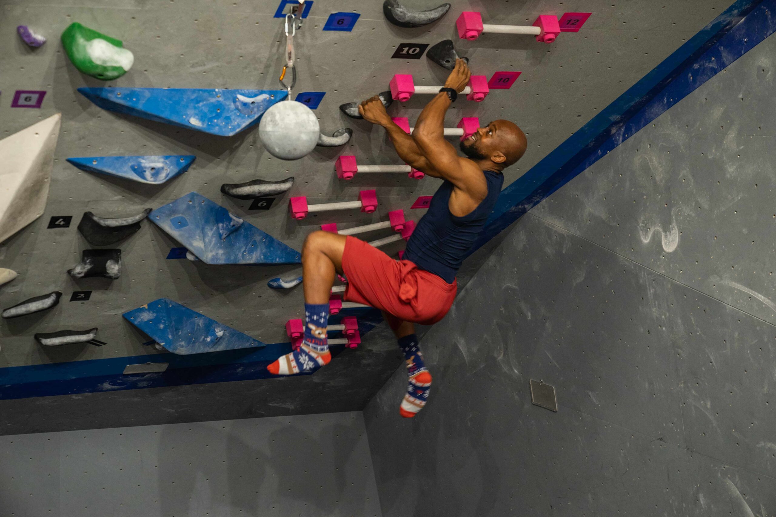 A man wearing silly socks campuses a bouldering wall.