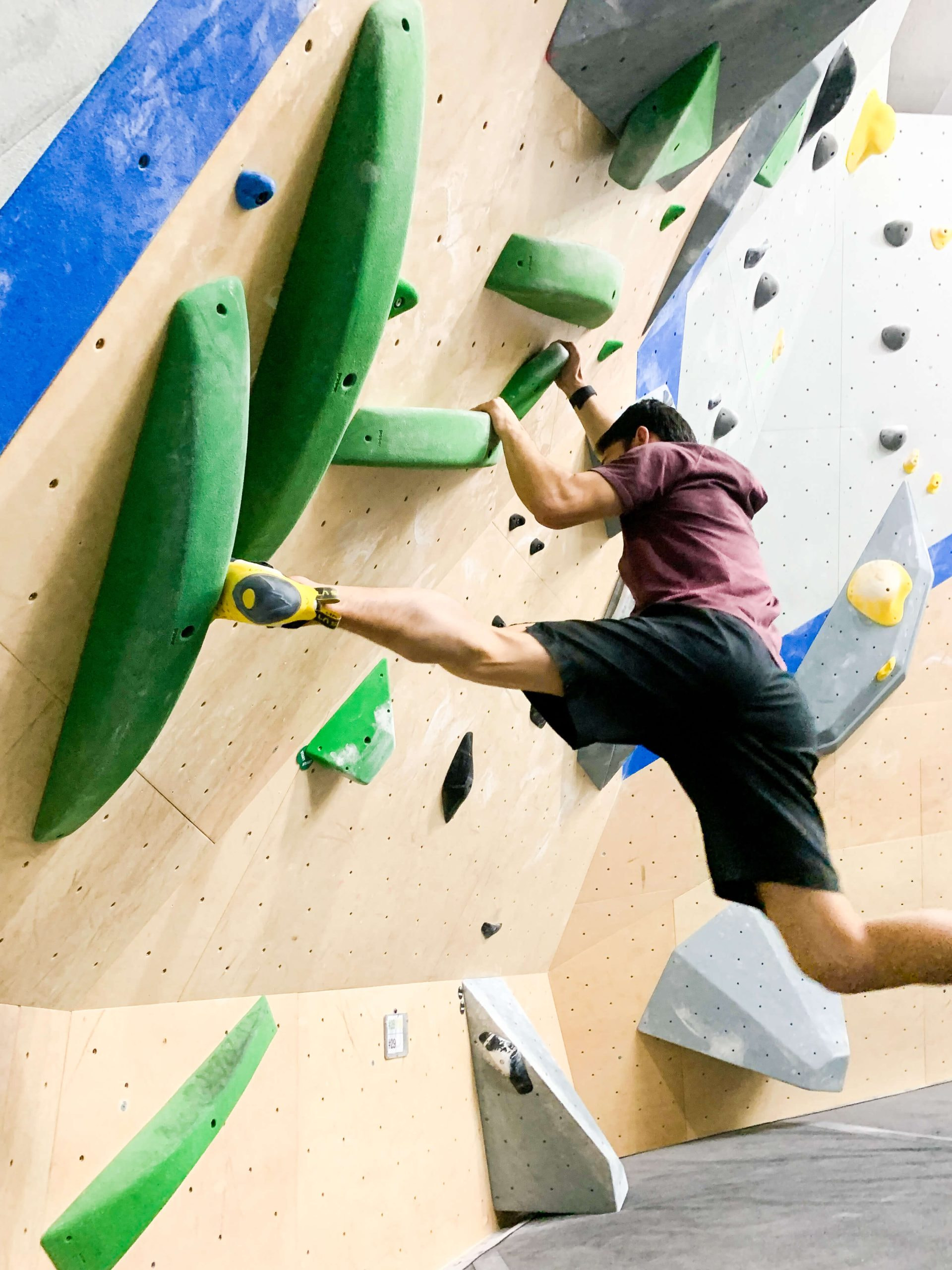 A young man is bouldering and is fighting a barndoor after making a dynamic move on the wall. His foot is flying behind him and he has a lot of momentum.