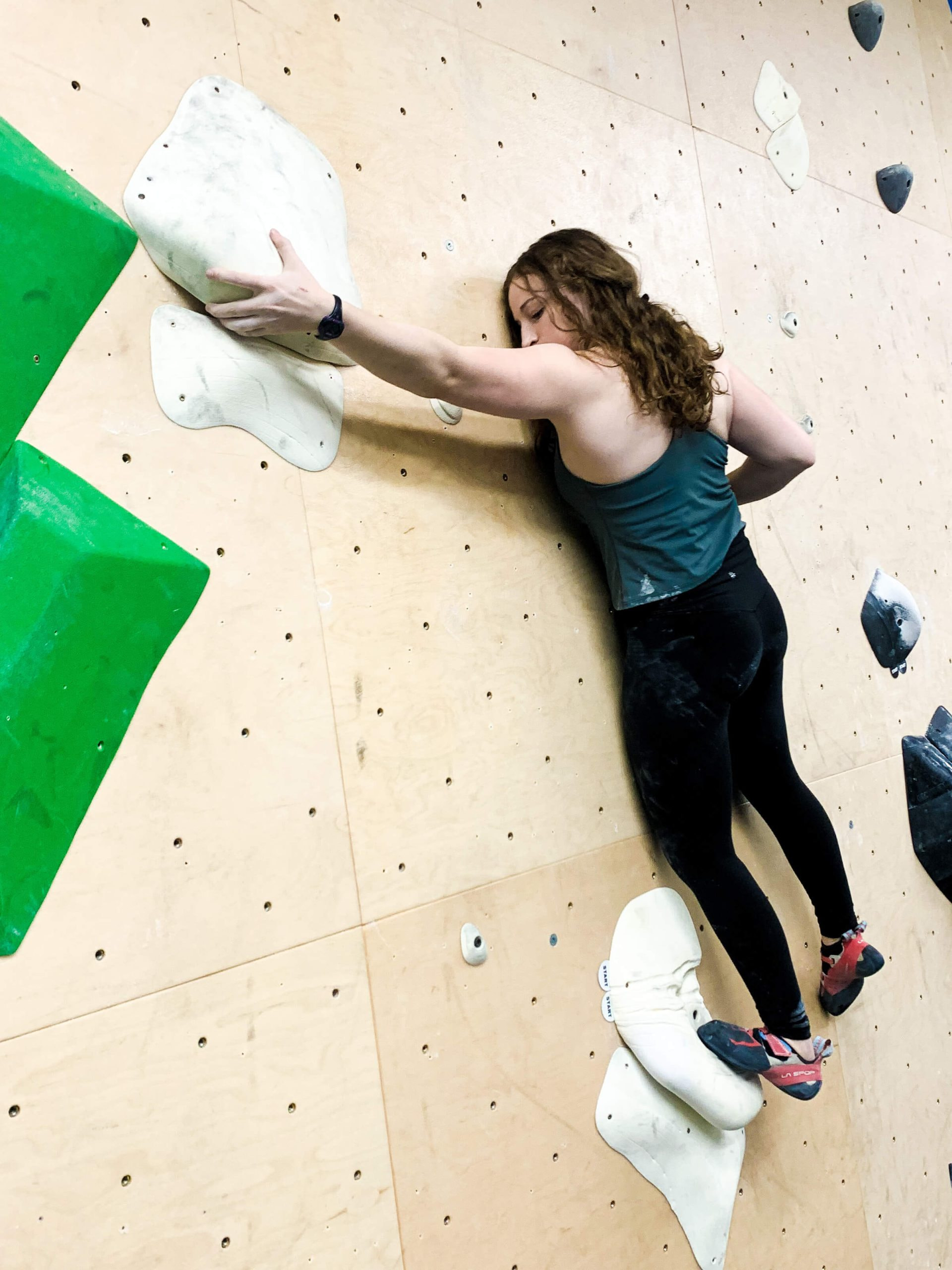 A young woman is grabbing hold of a slopey undercling as she balances over one foot on a slab climb.