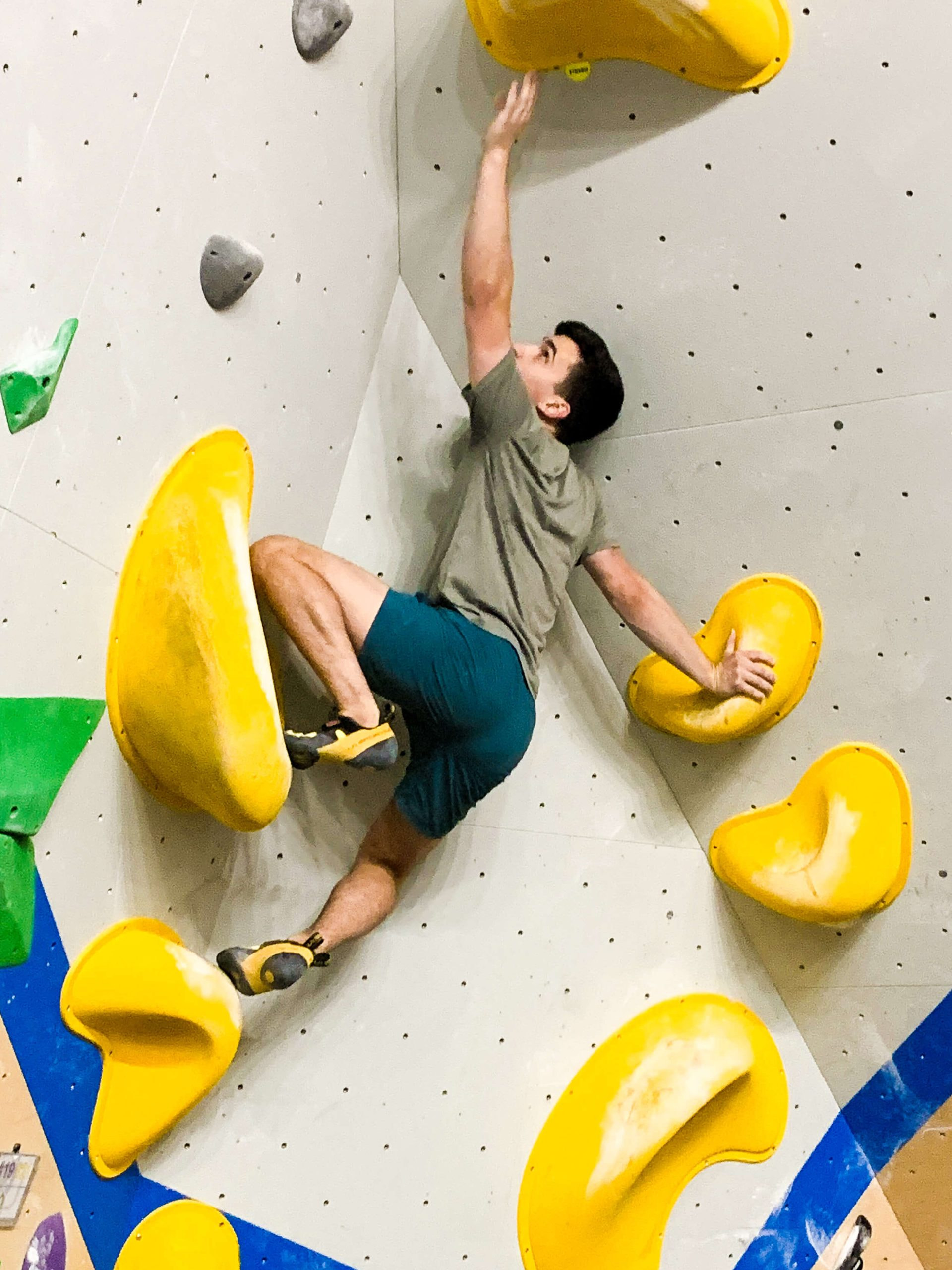 A man is mantling up over a large hold in a dihedral climb while reaching overhead for the next hold.
