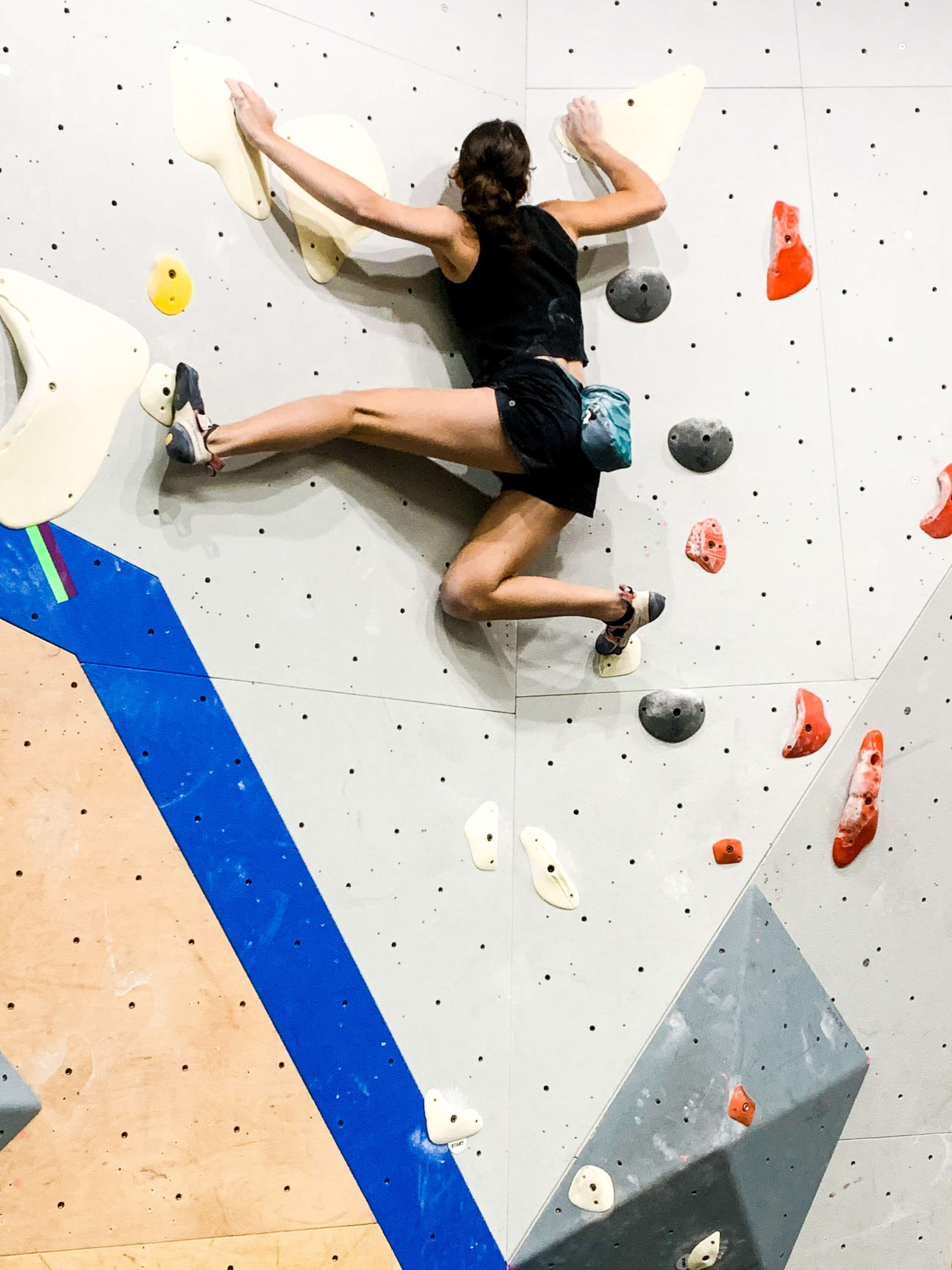 A woman is bouldering and has a deep drop knee on the wall with the other leg out straight.