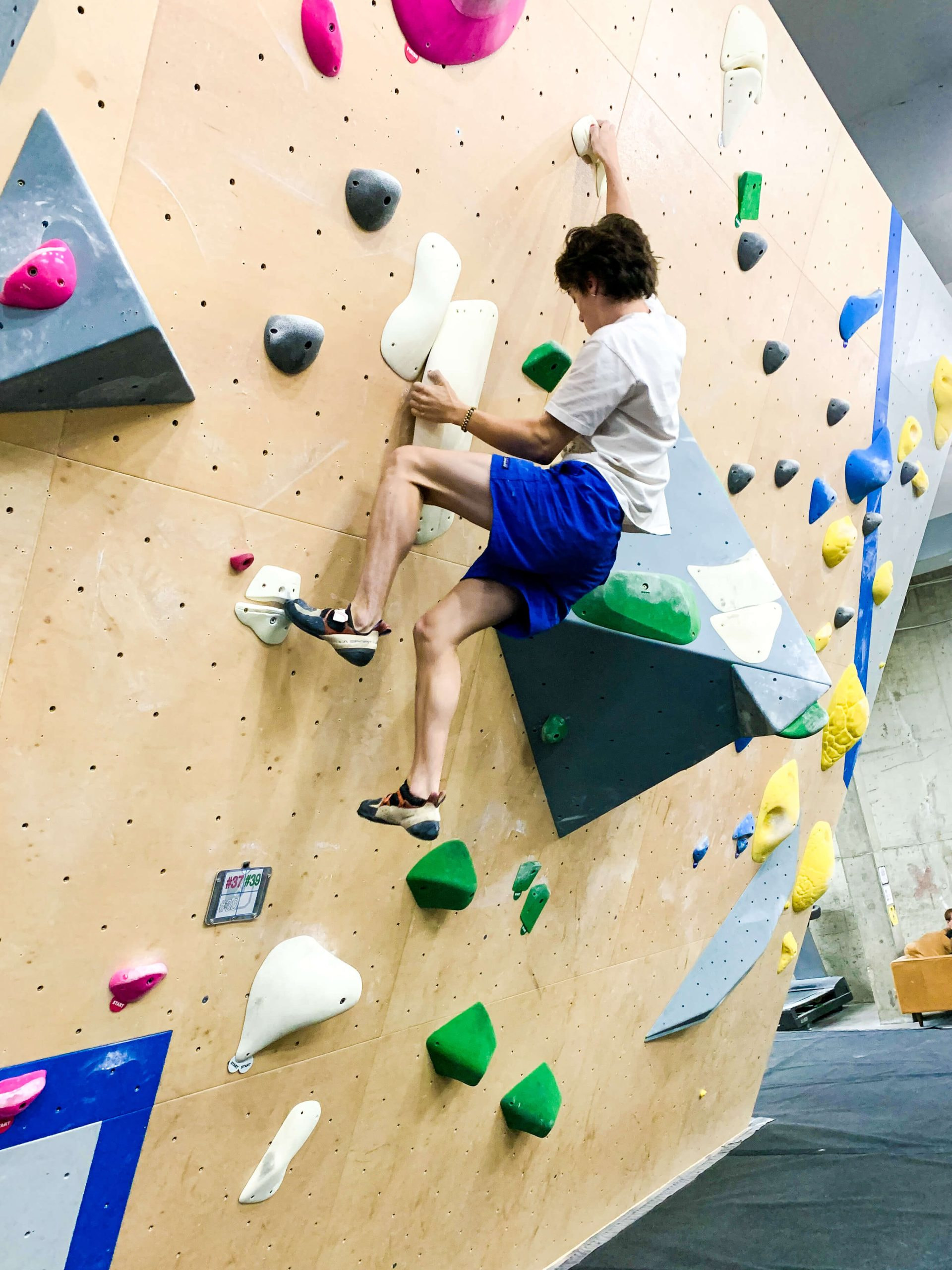 A young man is bouldering and holding onto a sidepull.