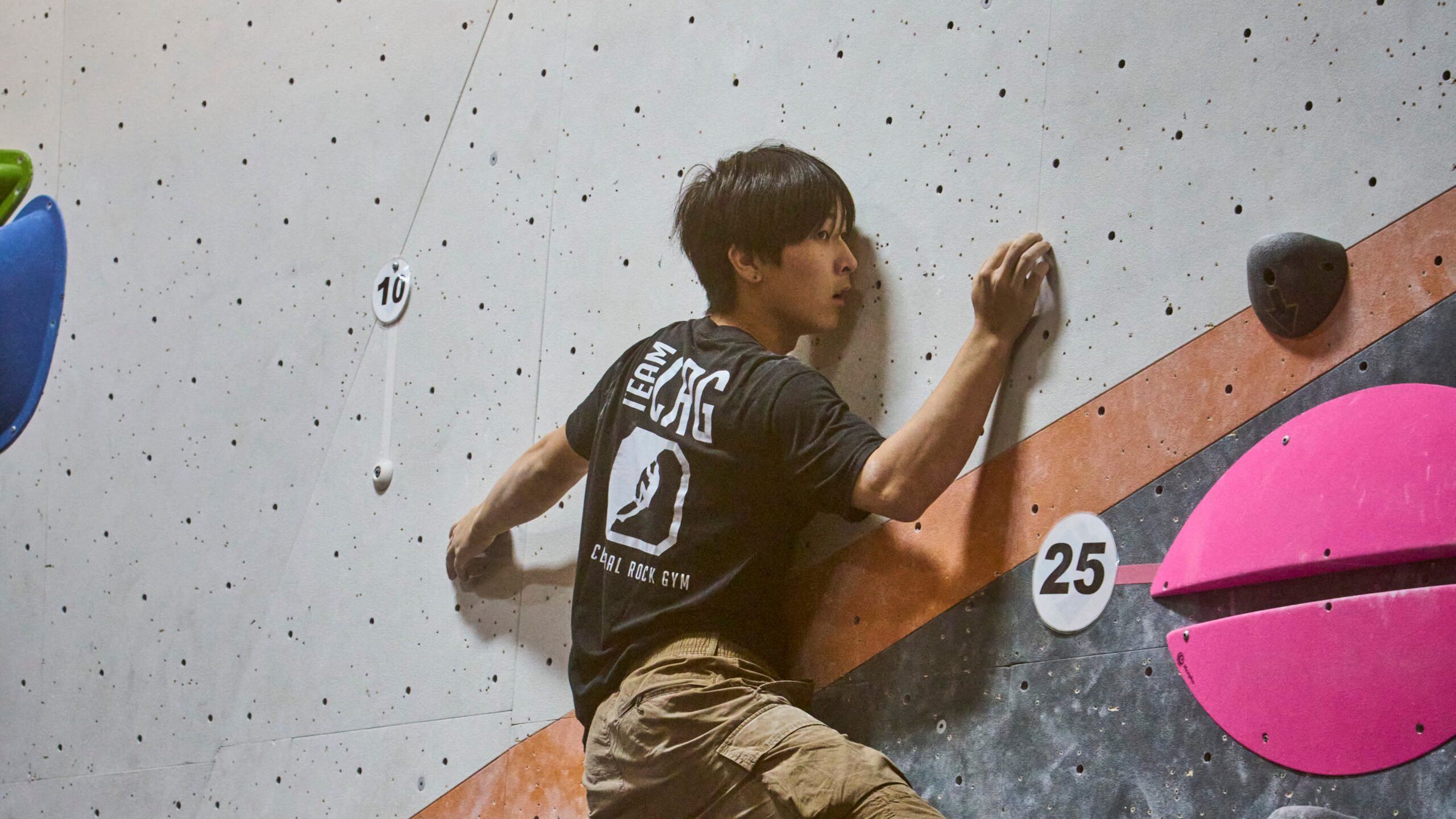 A teen boy wearing a competitive CRG team tshirt balances on a slabby boulder.