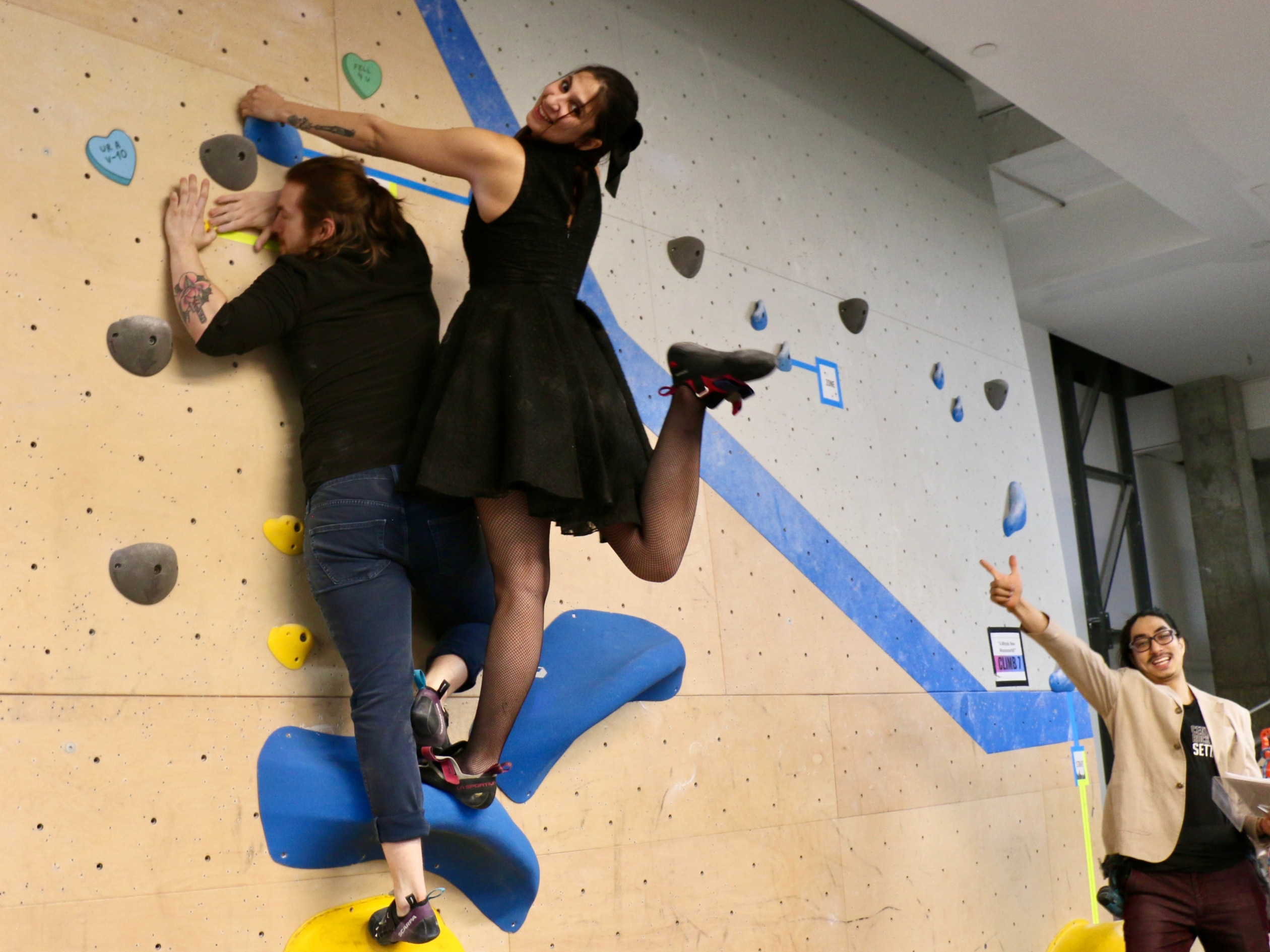 a couple completes a partner climb and poses for the camera, the judge points at them and smiles to the camera