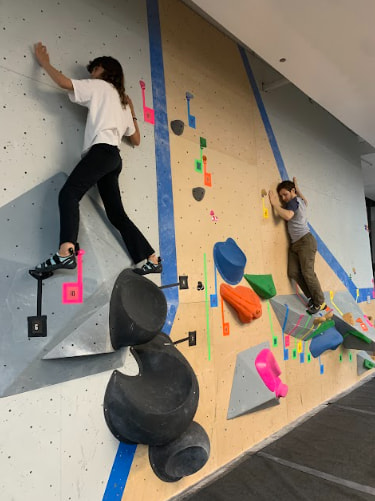 Two climbers, a woman and a man, are pictured on the bouldering wall on no hands climbs.