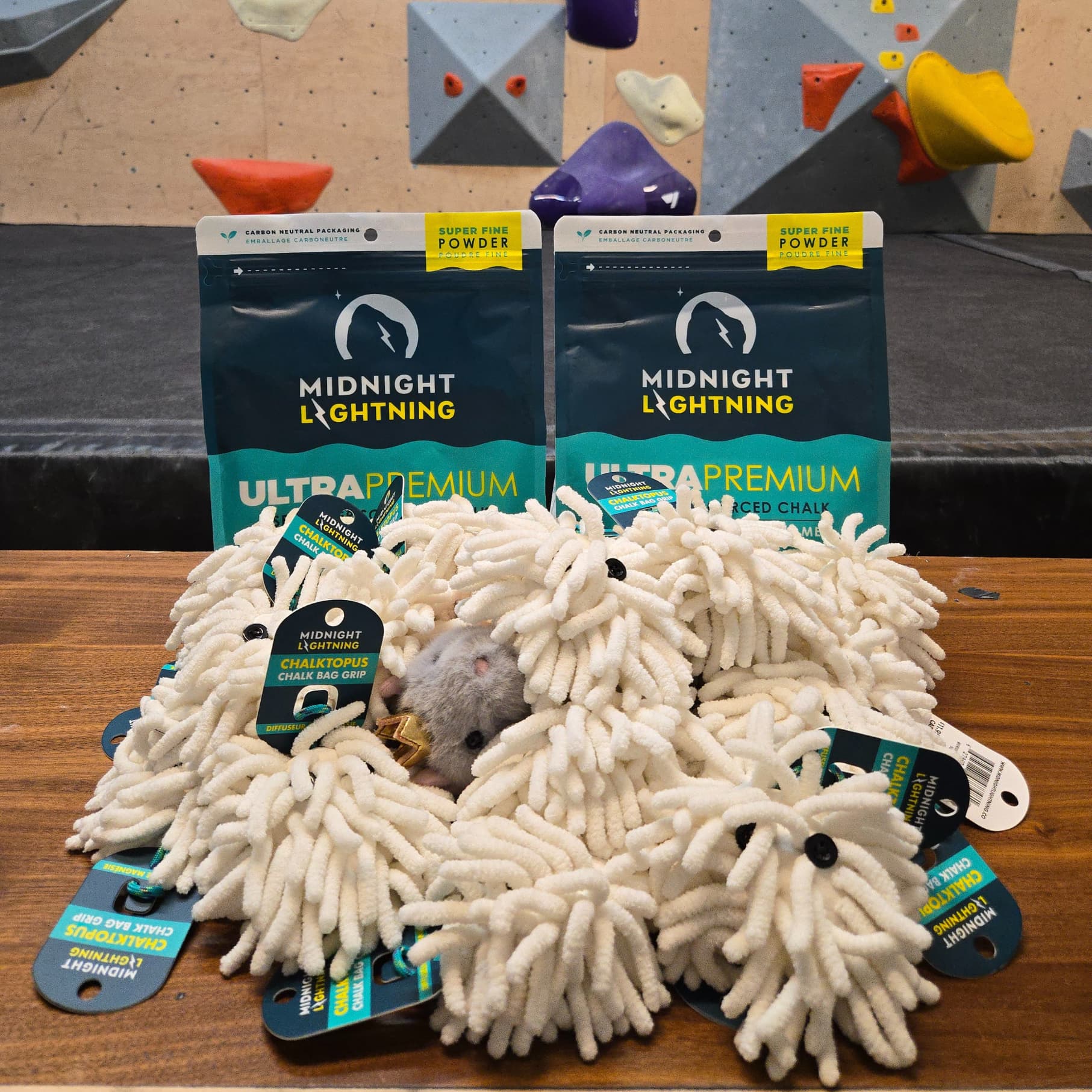 Prizes provided by Midnight Lightning arranged on a bench in front of the bouldering wall. Prizes include climbing chalk and the chalktopus product.