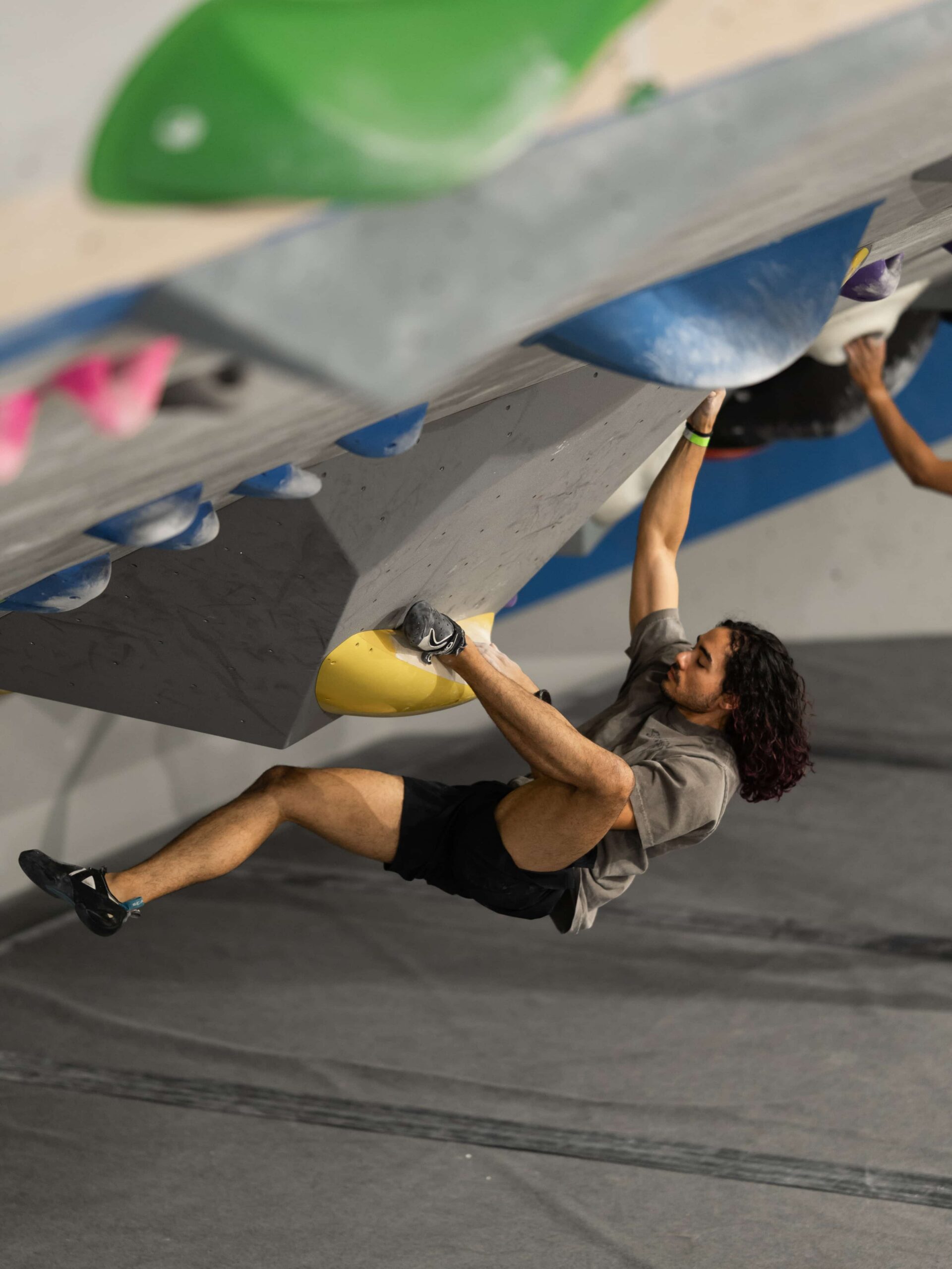 A man with long hair places a heel hook on a steep boulder during a community climbing competition.