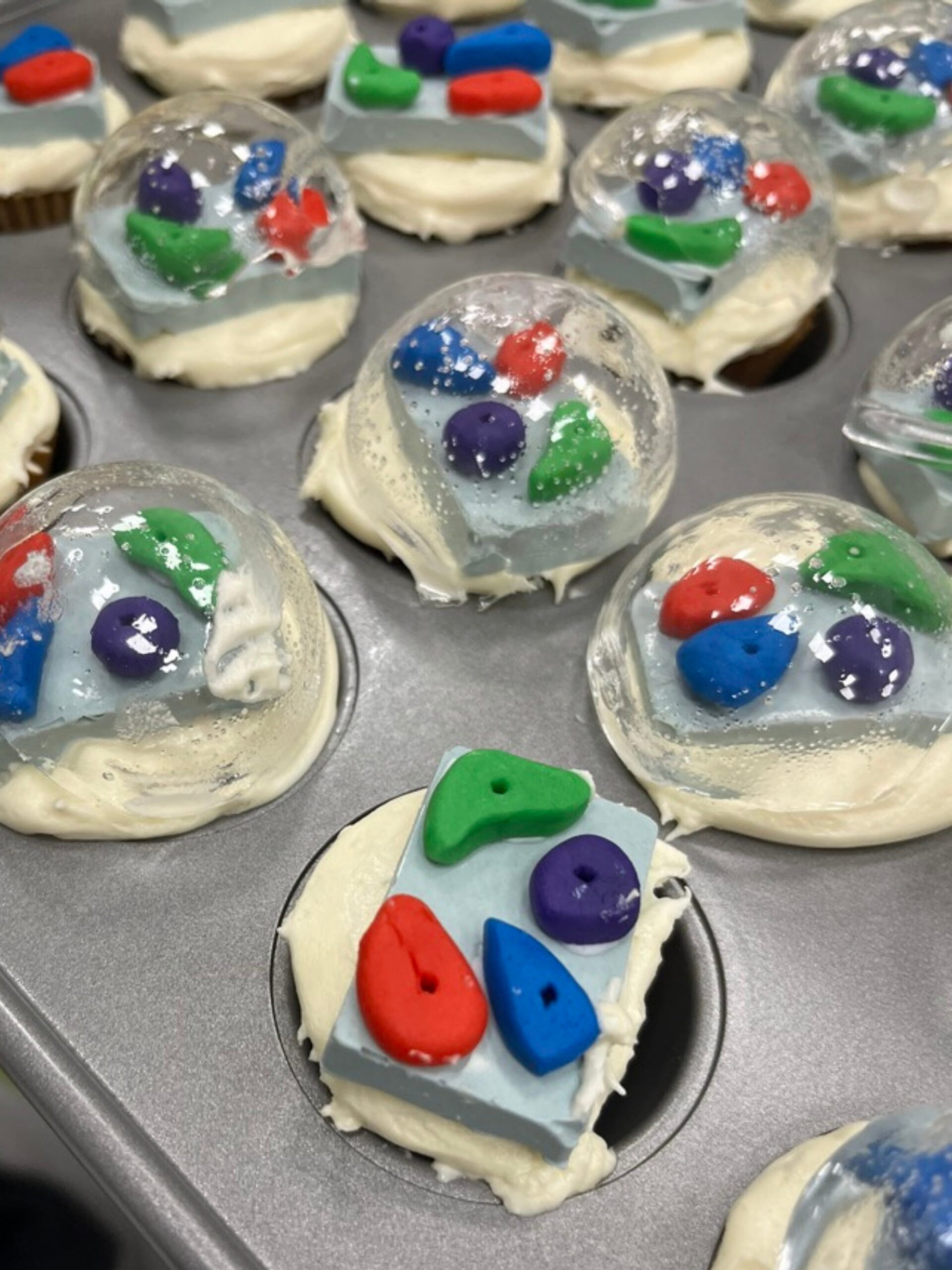 A cupcake tray. The cupcakes are decorate with chocolate pieces molded and colored like climbing holds and covered with a sugar globe.