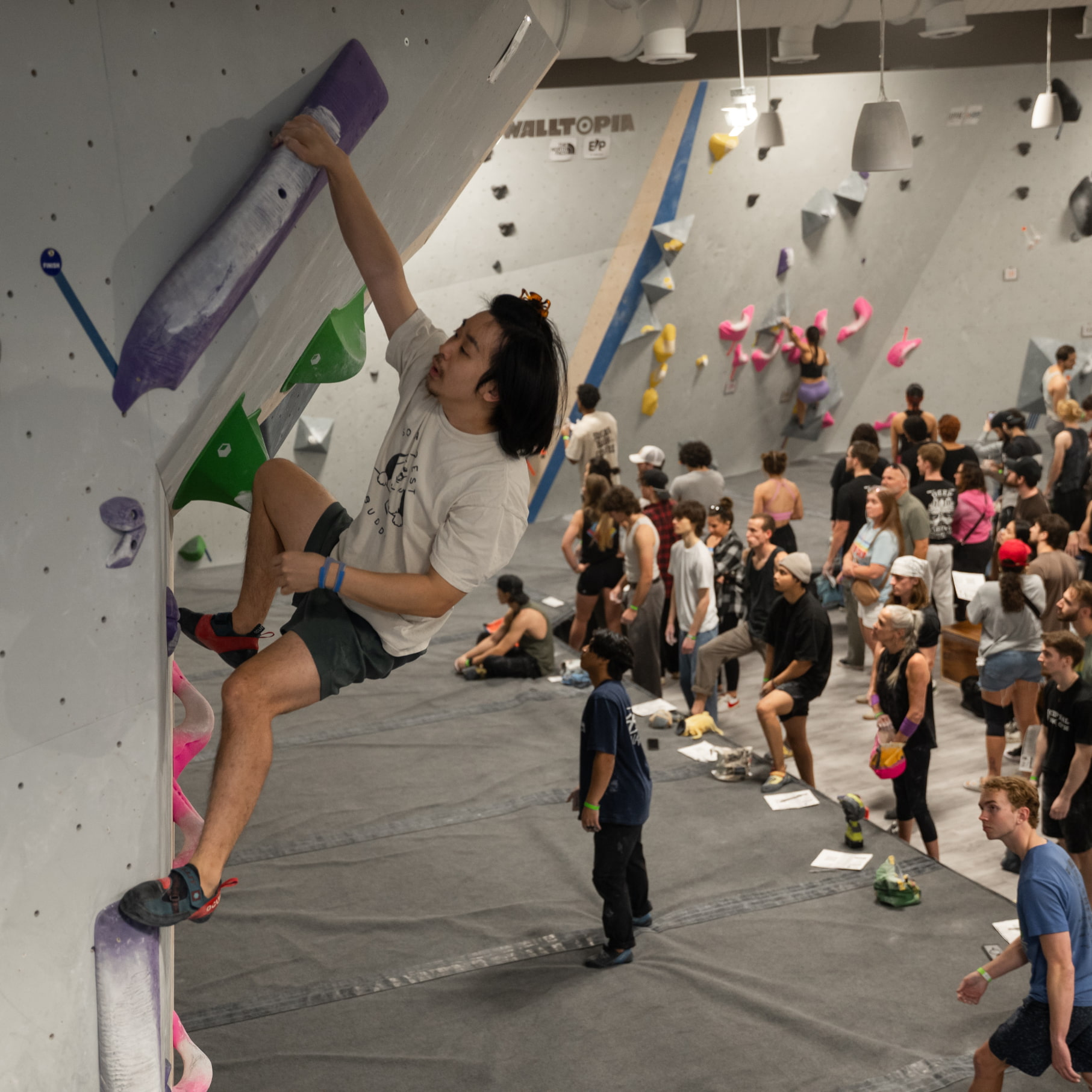A man with shoulder length hair grabs ahold of the finish hold, a tufa set at a 45 degree angle on the overhung portion of the bouldering wall.