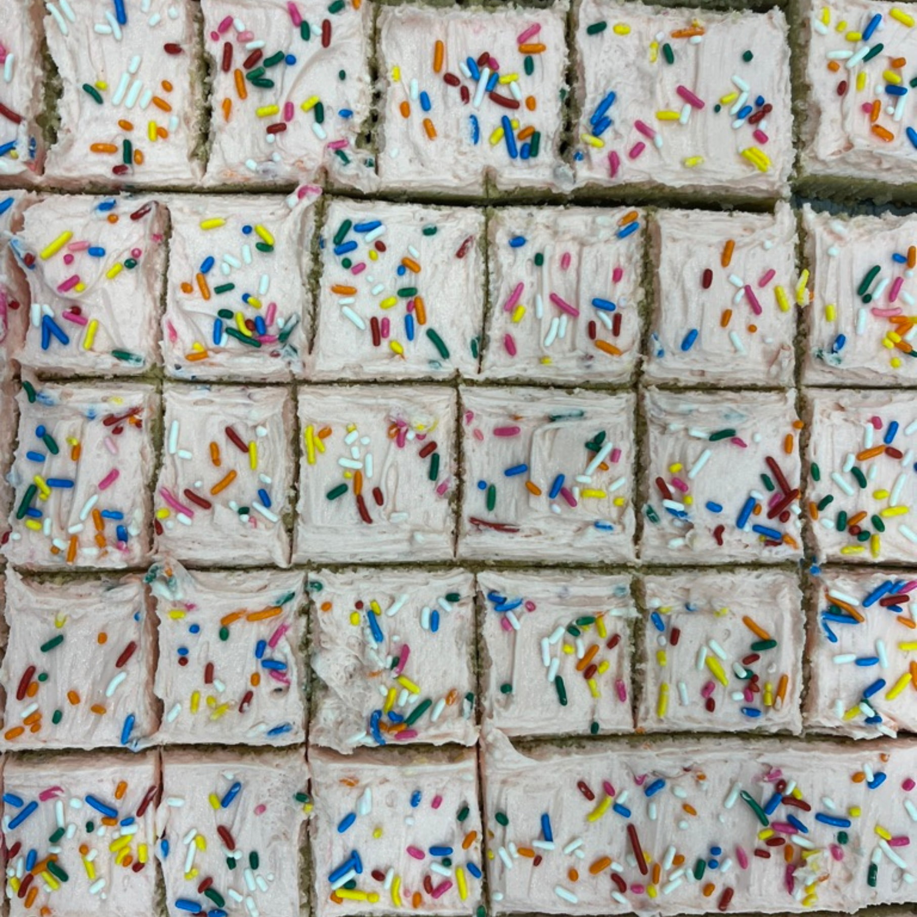 A tray full of baked bars slathered with icing and covered in sprinkles