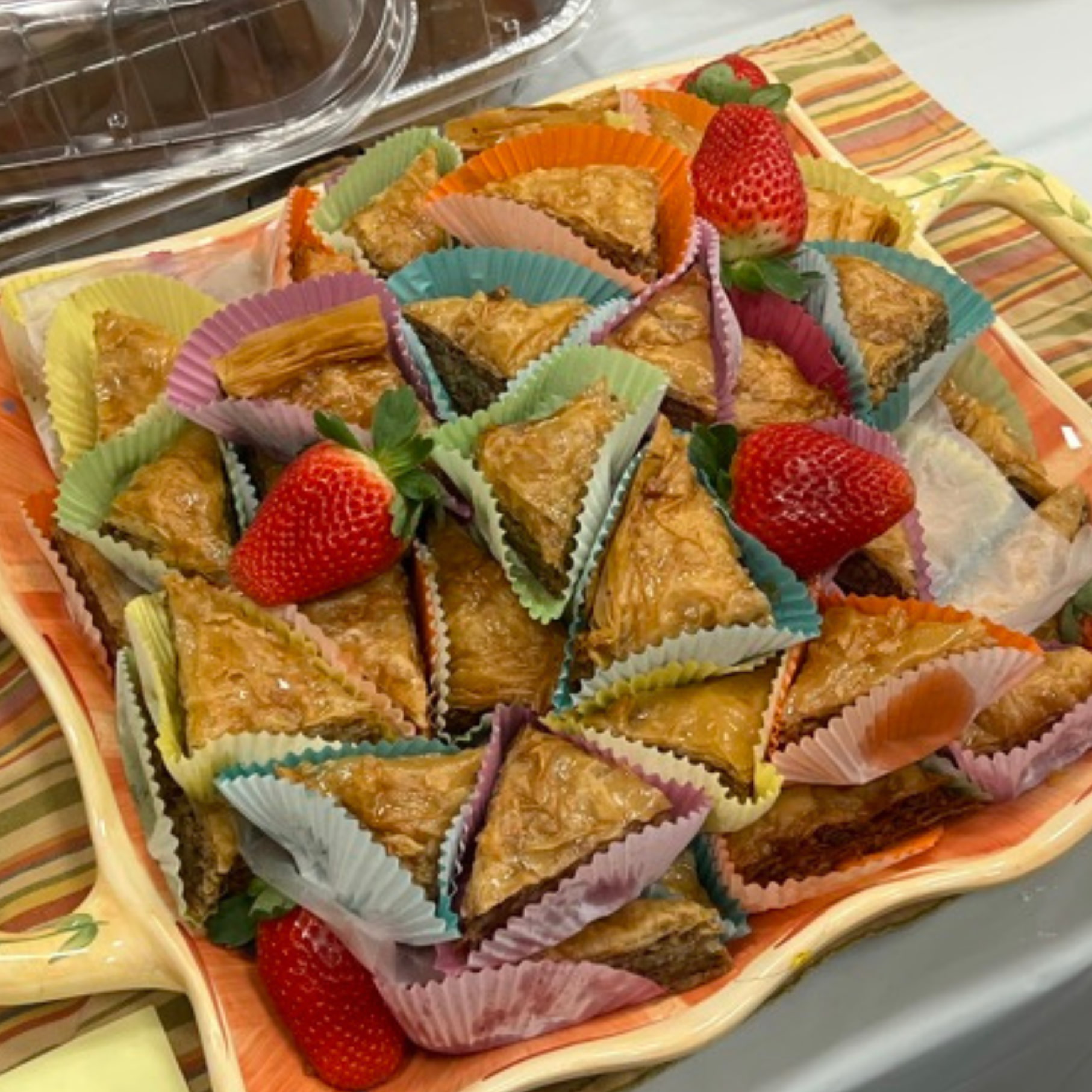 A tray full of baklava triangles garnished with whole strawberries.