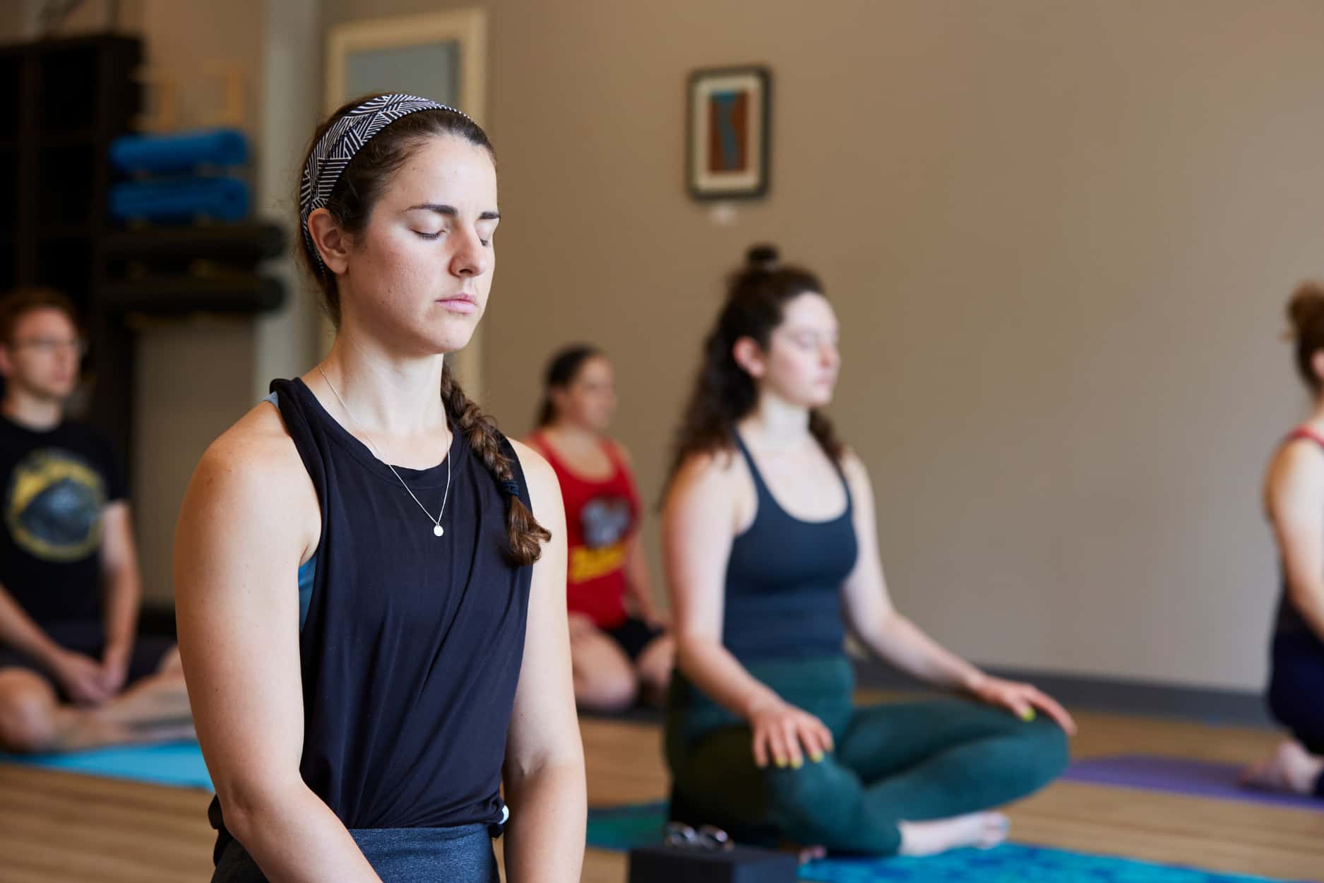 A class sits on their yoga mats with eyes closed as they observe their breathing and prepare for the class.