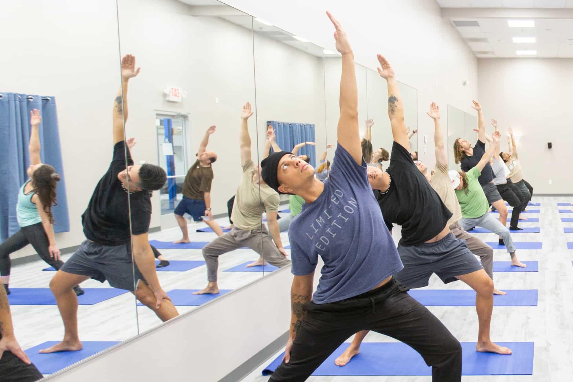A yoga class reverses their warrior 2 pose. The mirror behind them reflects the pose.