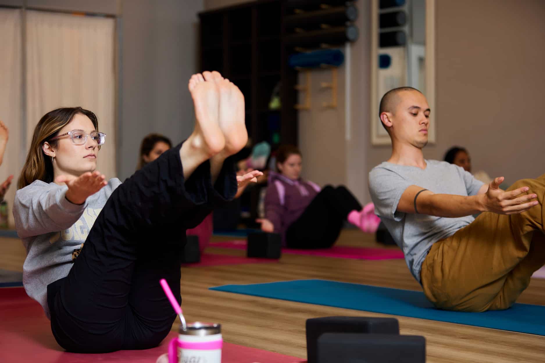 A yoga class holds boat pose together and focuses on finding a stable core during a class at Central Rock Gym.