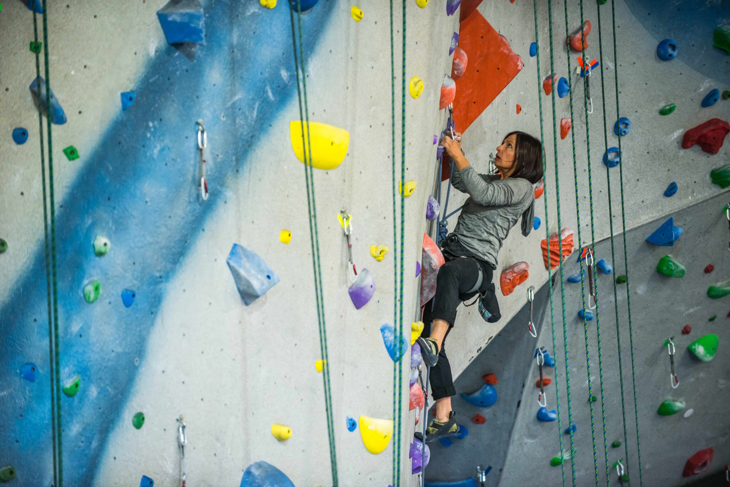 A women with short hair is lead climbing. She is just below the clip that the rope is clipped into.