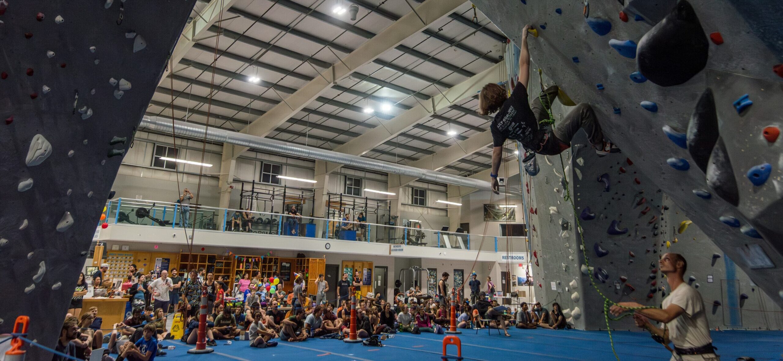 Person lead climbing at a competition with a large crowd watching.