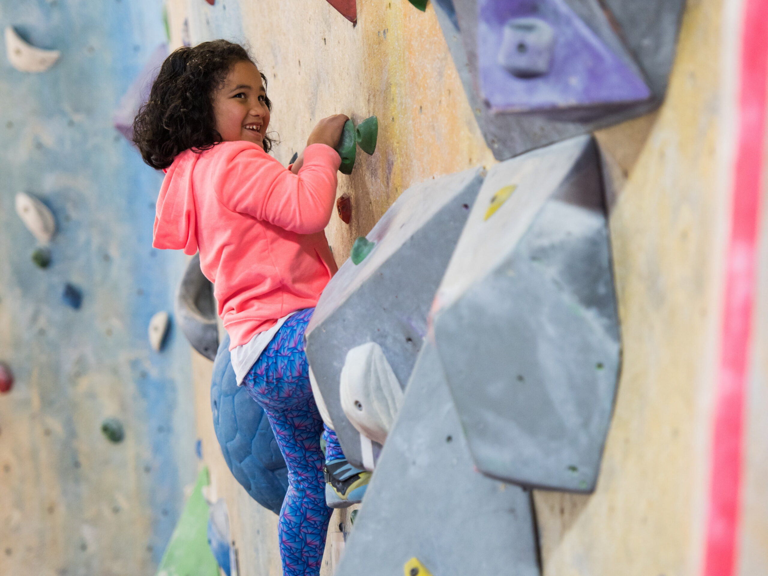 A young girl bouldering on an indoor rock climbing wall.