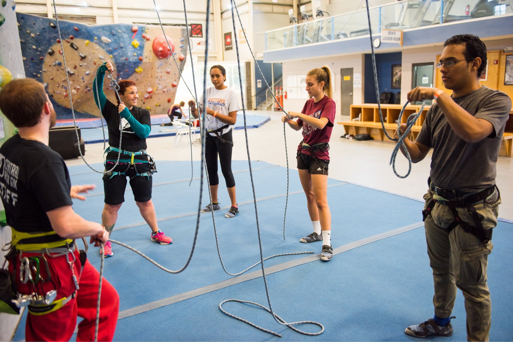 A group of young adults learning to tie a figure eight knot for top rope climbing. A CRG staff member is displaying what the knot should look like to the group.