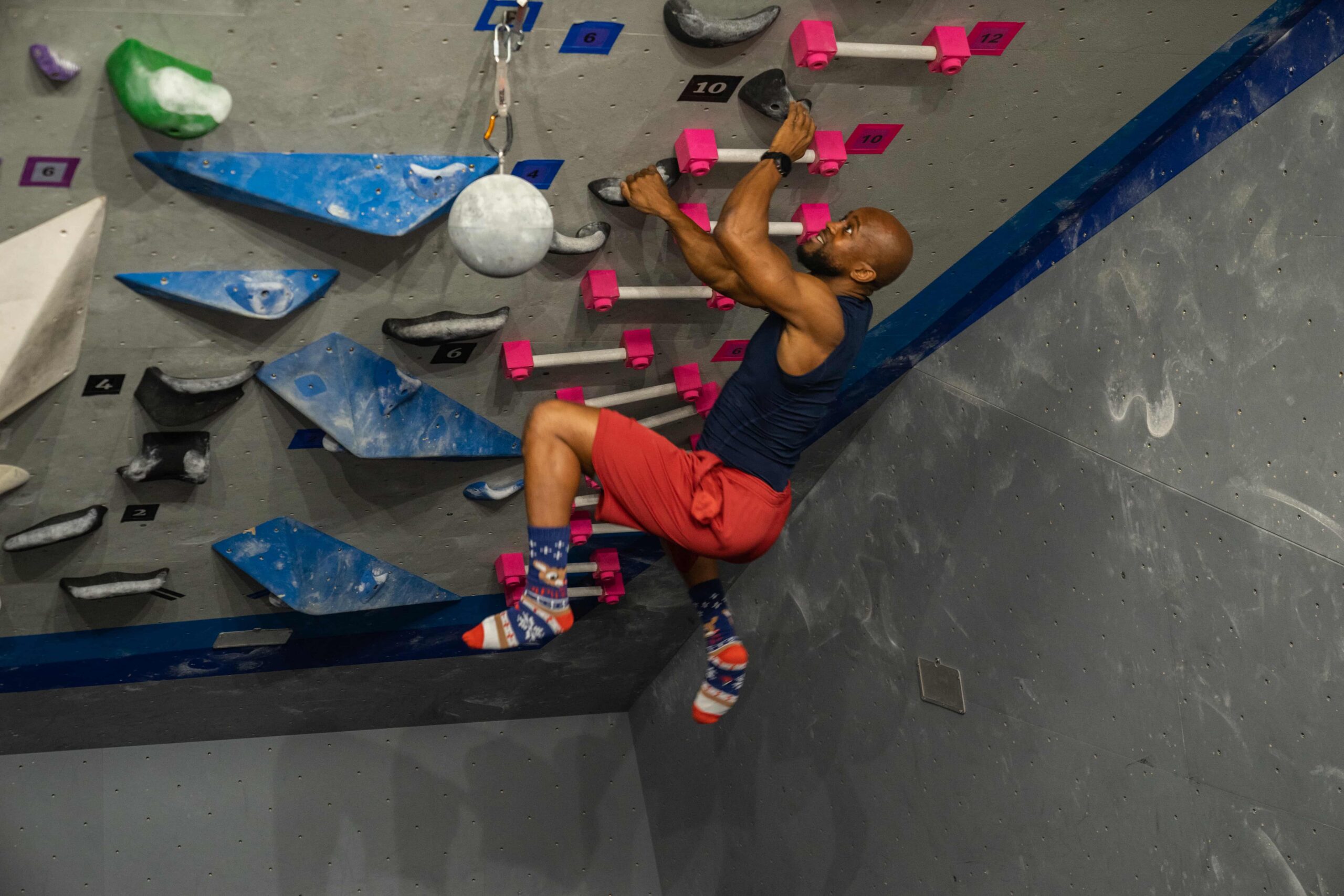 A man wearing silly socks campuses a bouldering wall.