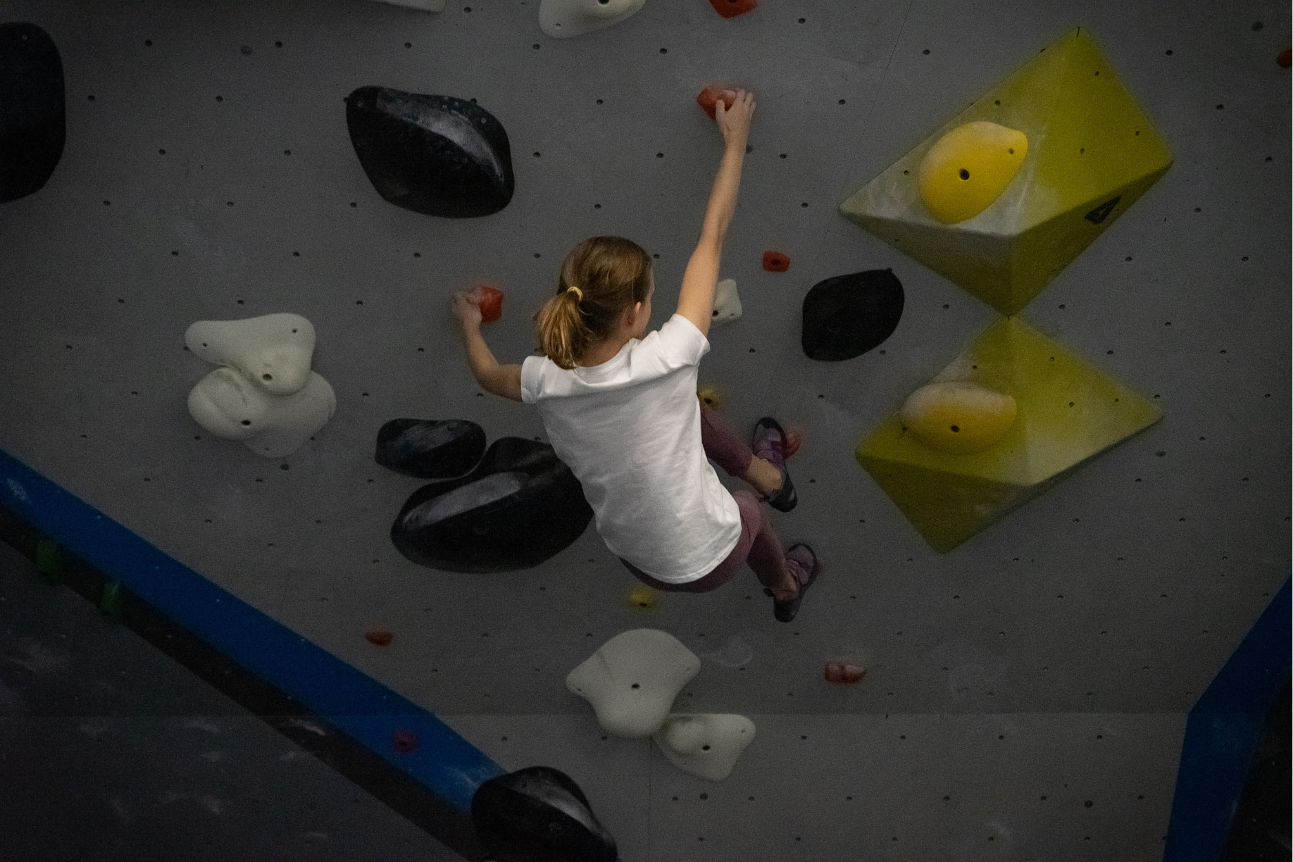 A girl holds onto a steep bouldering wall and steps her toes up higher on the wall.