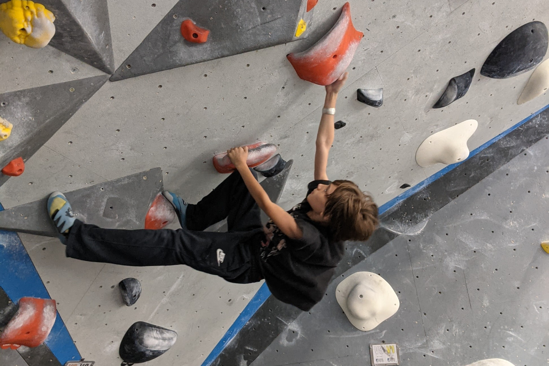 A young boy boulders on a very steep wall.