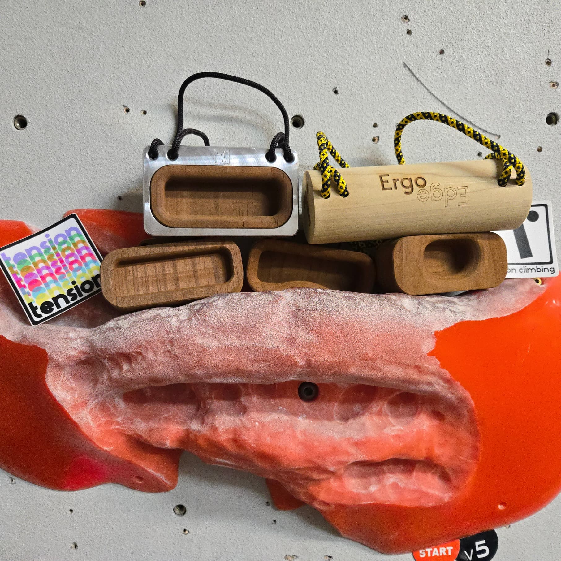 A number of Tension climbing products including the Ergo, stickers, and other training tools stacked on top of a climbing hold at Central Rock Gym Chelsea.