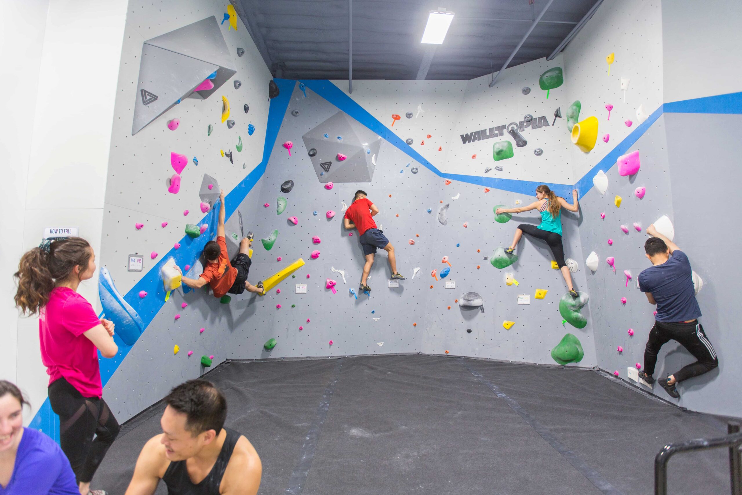 Several climbers work bouldering problems on the bright white walls at Central Rock Gym North Station while friends watch and chat below