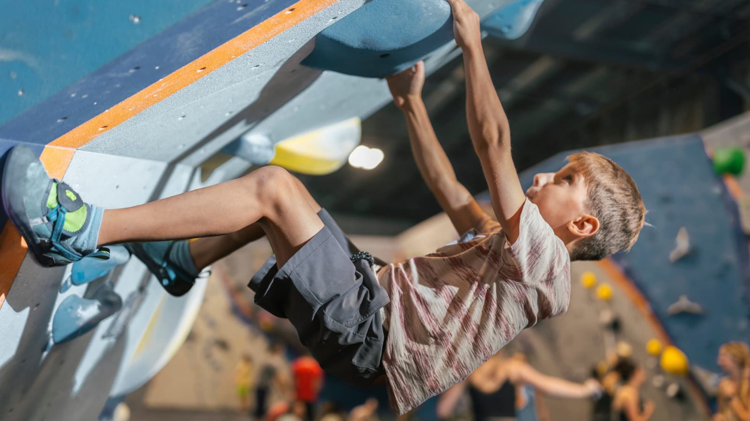 A young boy has a a focused face as he hangs onto the overhang and looks towards the next climbing hold.