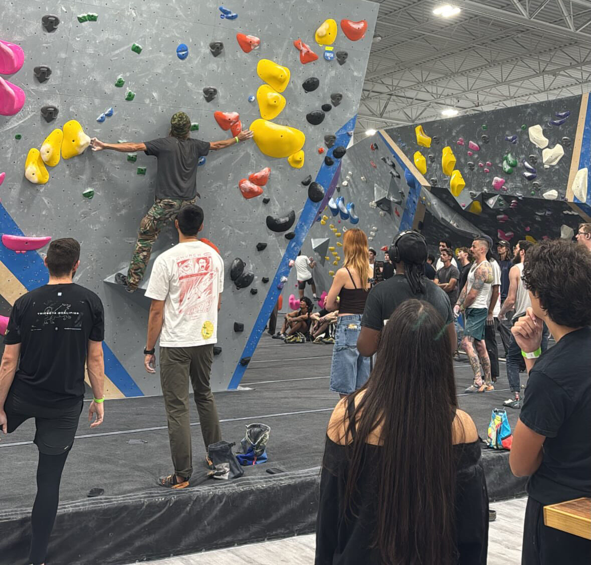people crowding around boulders watching a climber on a yellow route