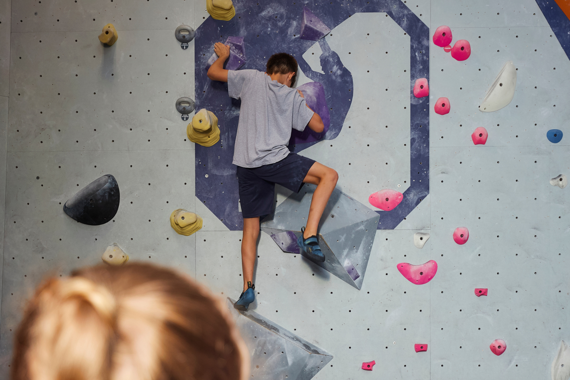 A young boy bouldering on top of the CRG logo.