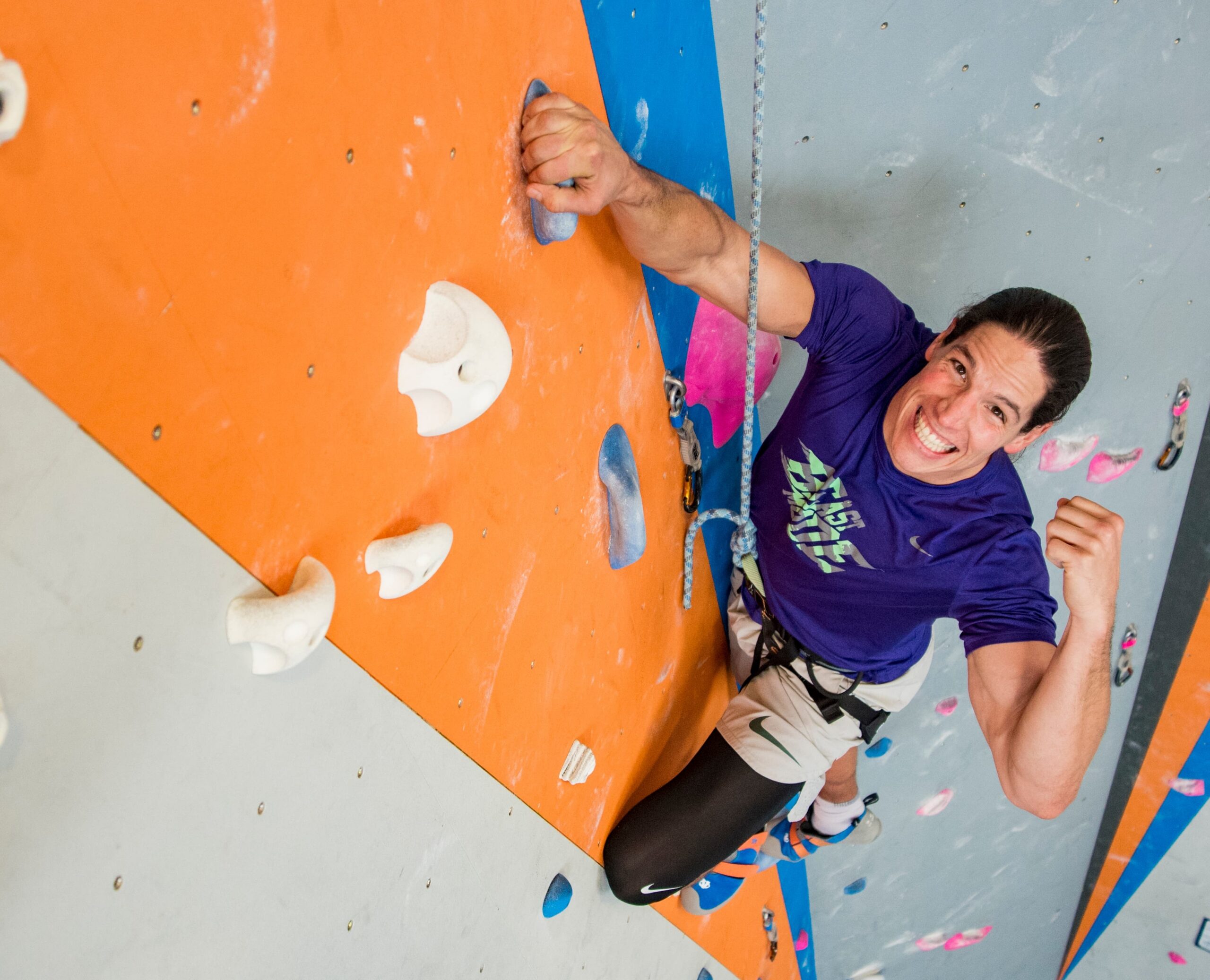 A lady climbing on a rope wall fistpumping and smiling big.