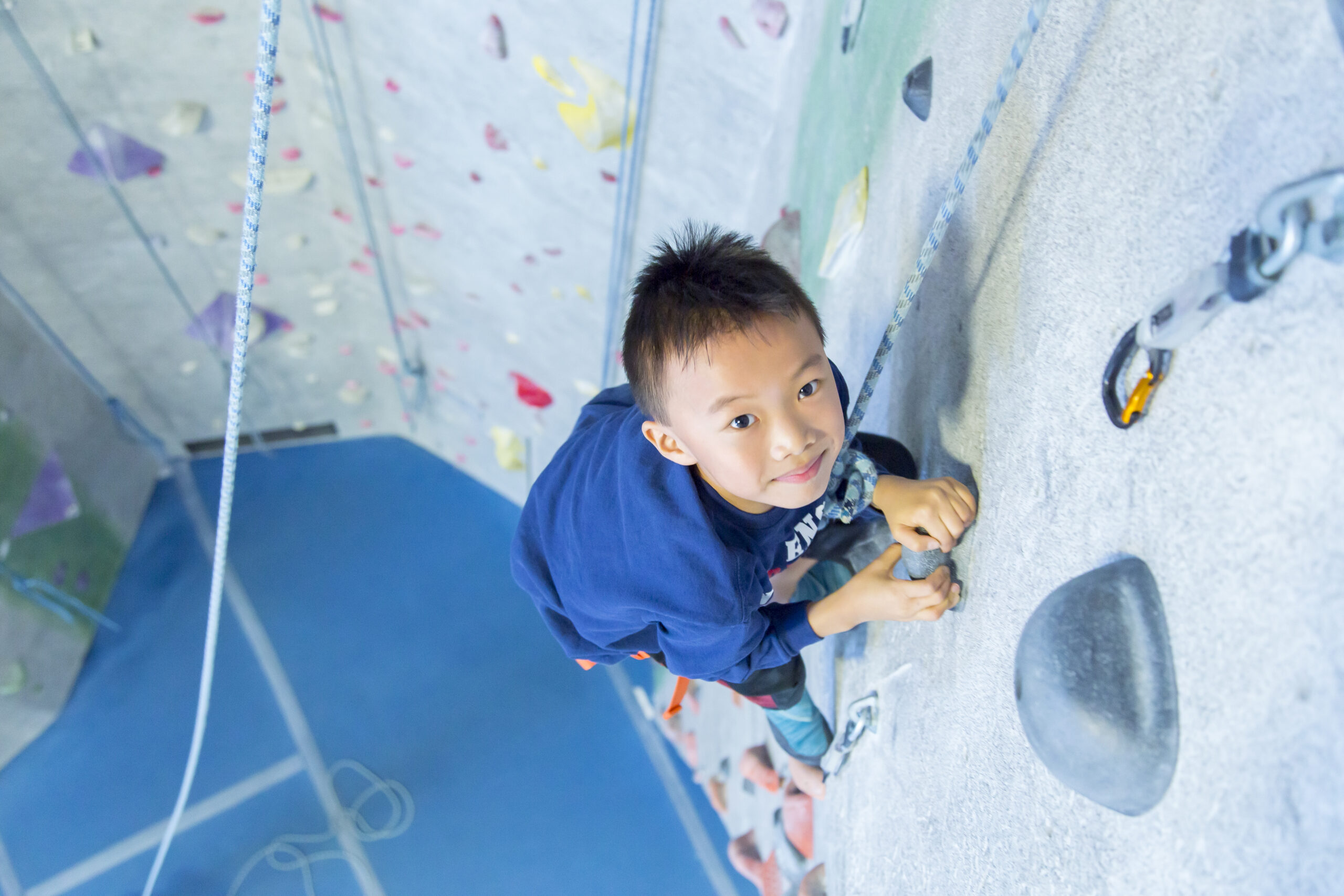 A young boy is top roping and looking up at the camera.
