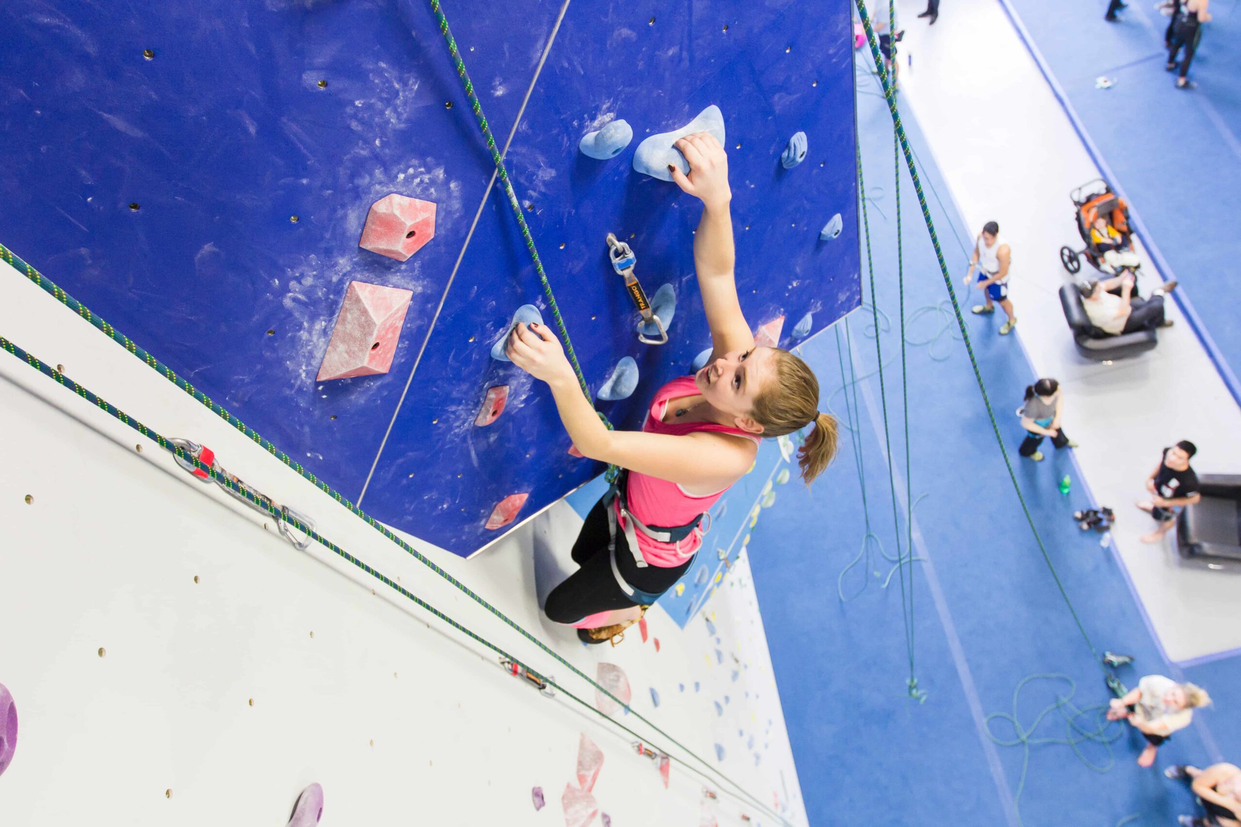 A teen girl looks up towards the next hold as she top rope climbs.
