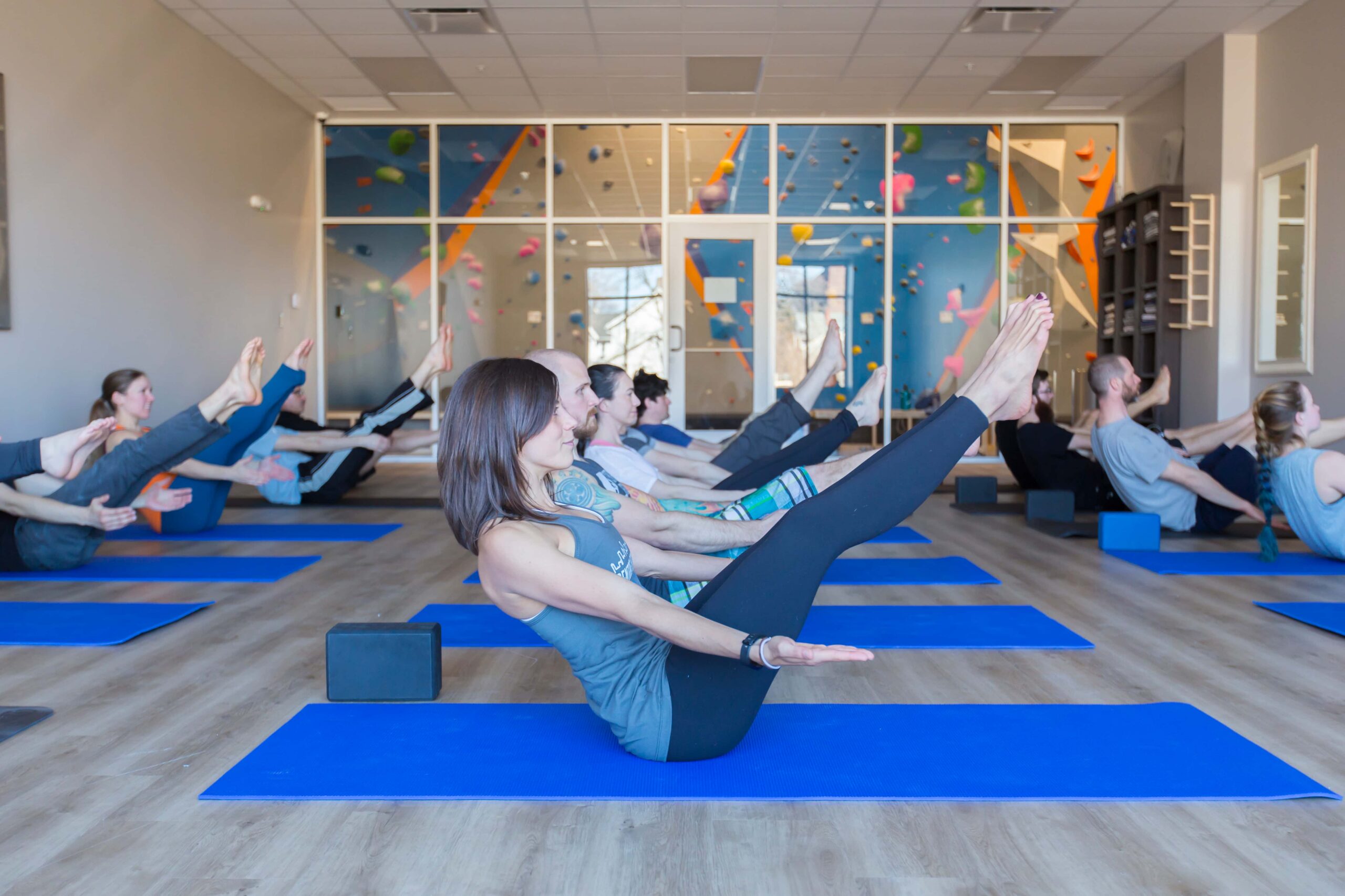 A yoga class sits in boat pose.