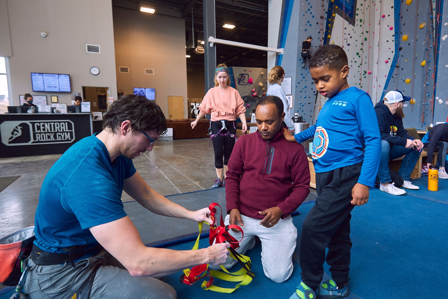 Volunteer assists adaptive climber in putting on their harness during private climbing session.