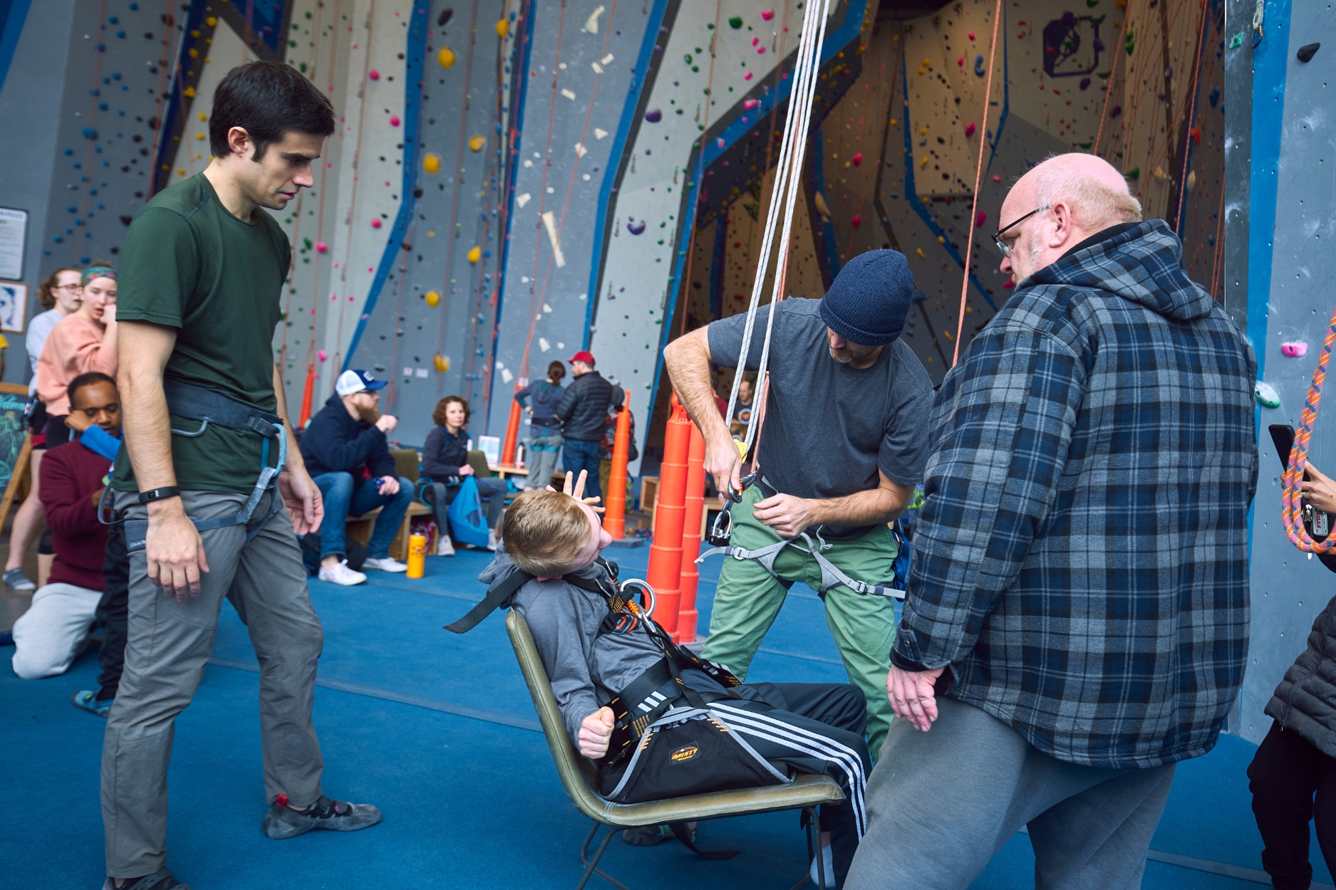 Adaptive Climbing Volunteers work to together to set up the easy seat for an Adaptive Climber, during an Adaptive Climbing Day.
