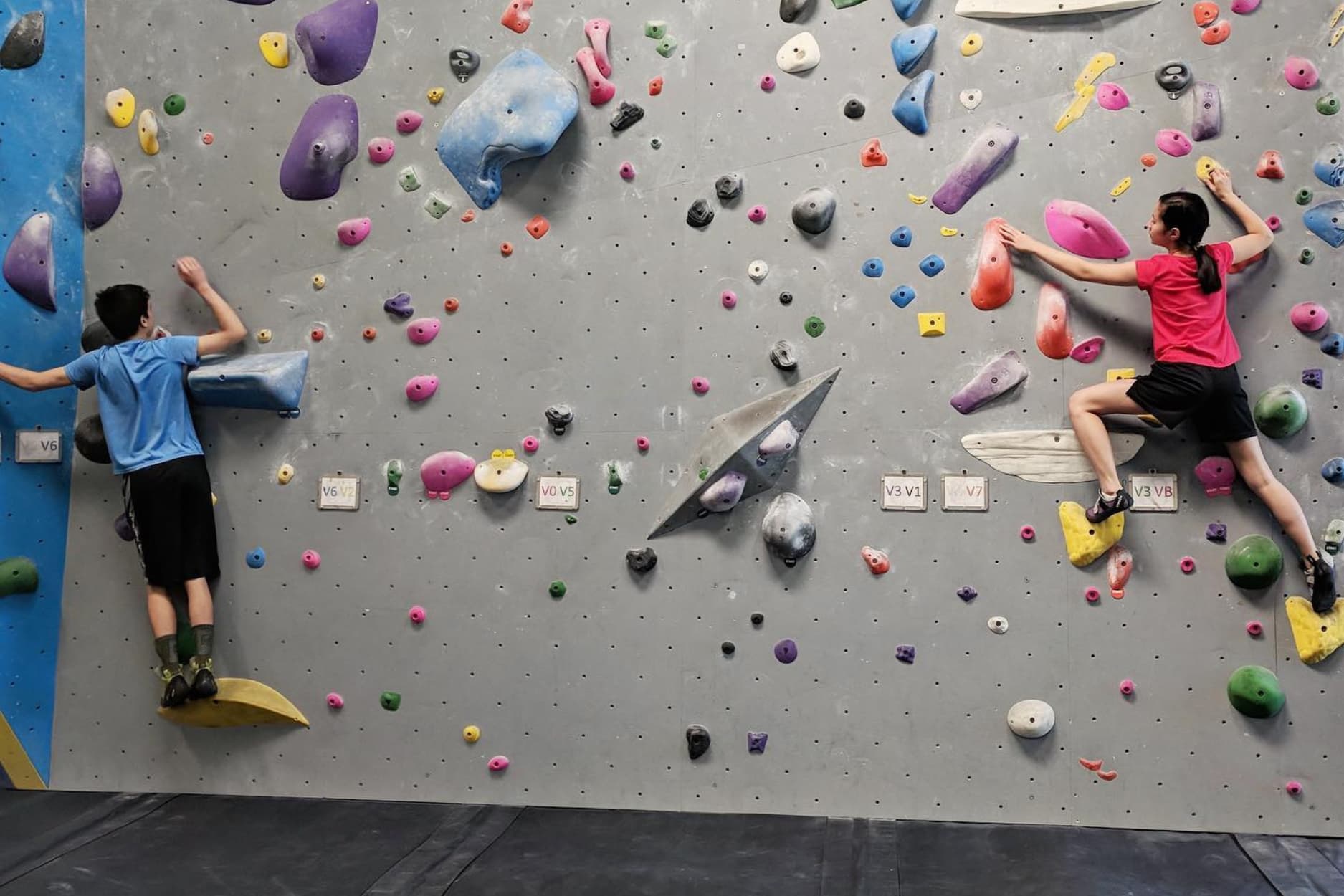 Two young children ( a boy and girl) boulder on a vertical wall.