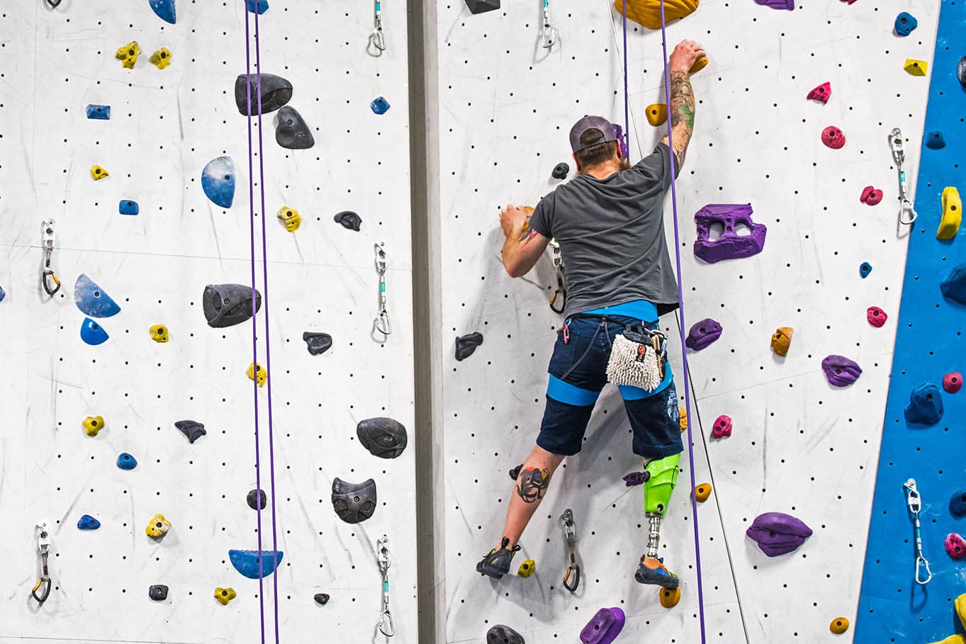 A paraclimber with a prosthetic leg ascends the rope climbing wall during an Adaptive Climbing Event.