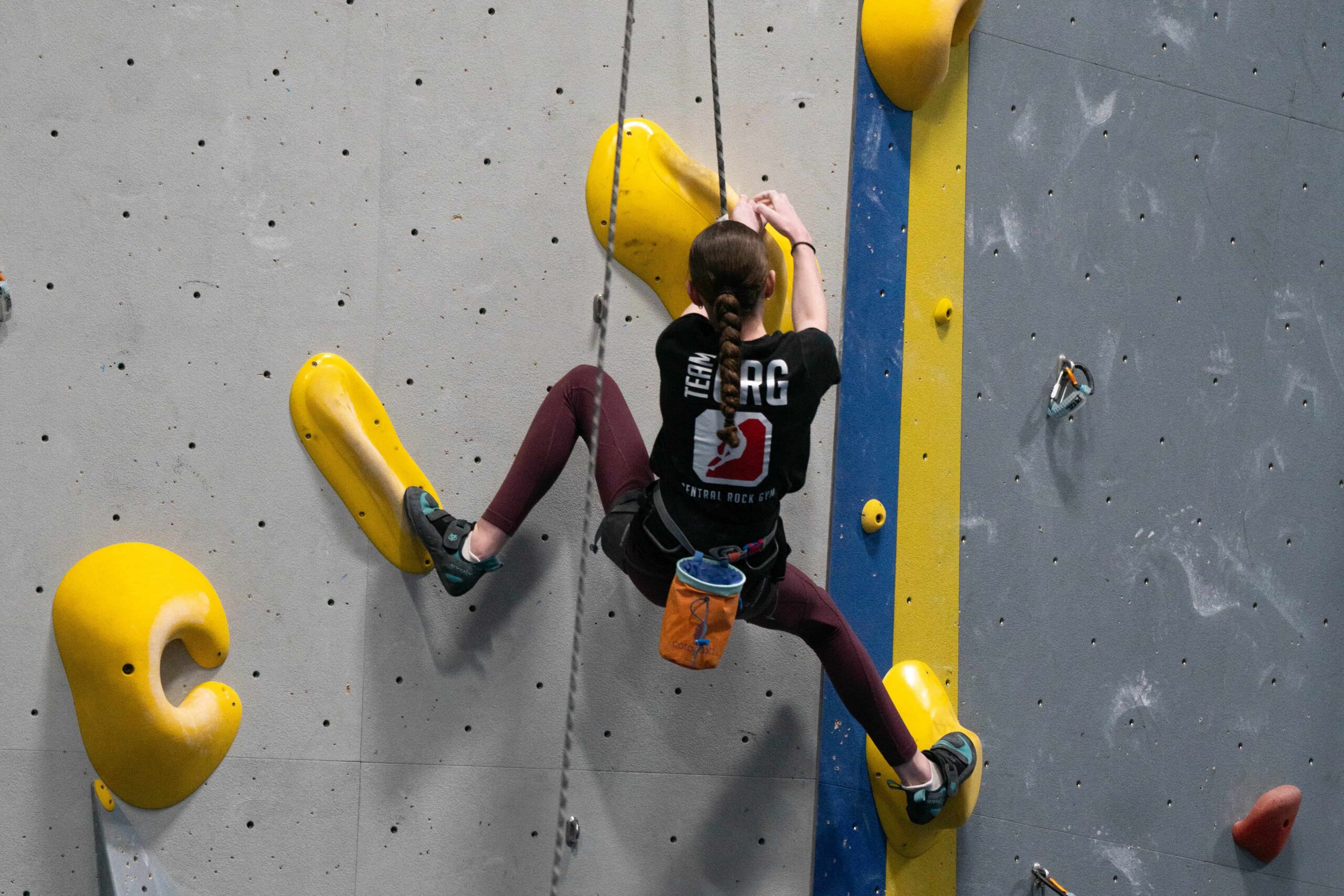 Pre-teen girl in a black CRG Stoneham team t-shirt top ropes a yellow route at a competition