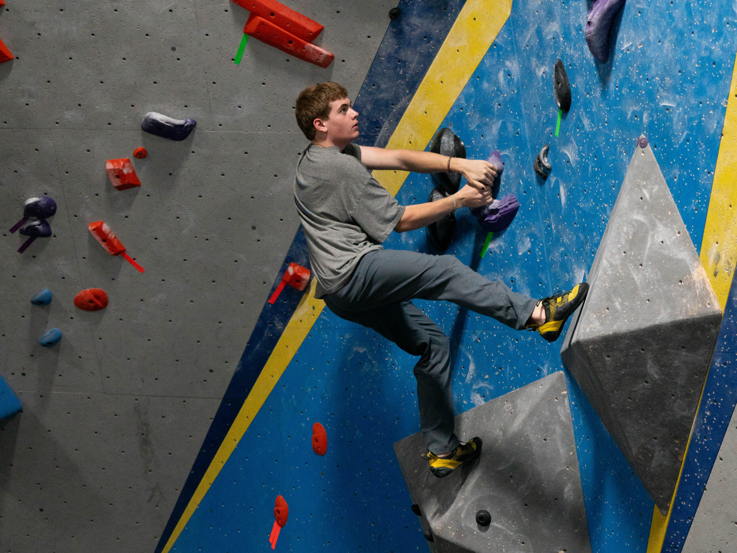 A teenager in a grey shirt boulders at CRG Stoneham