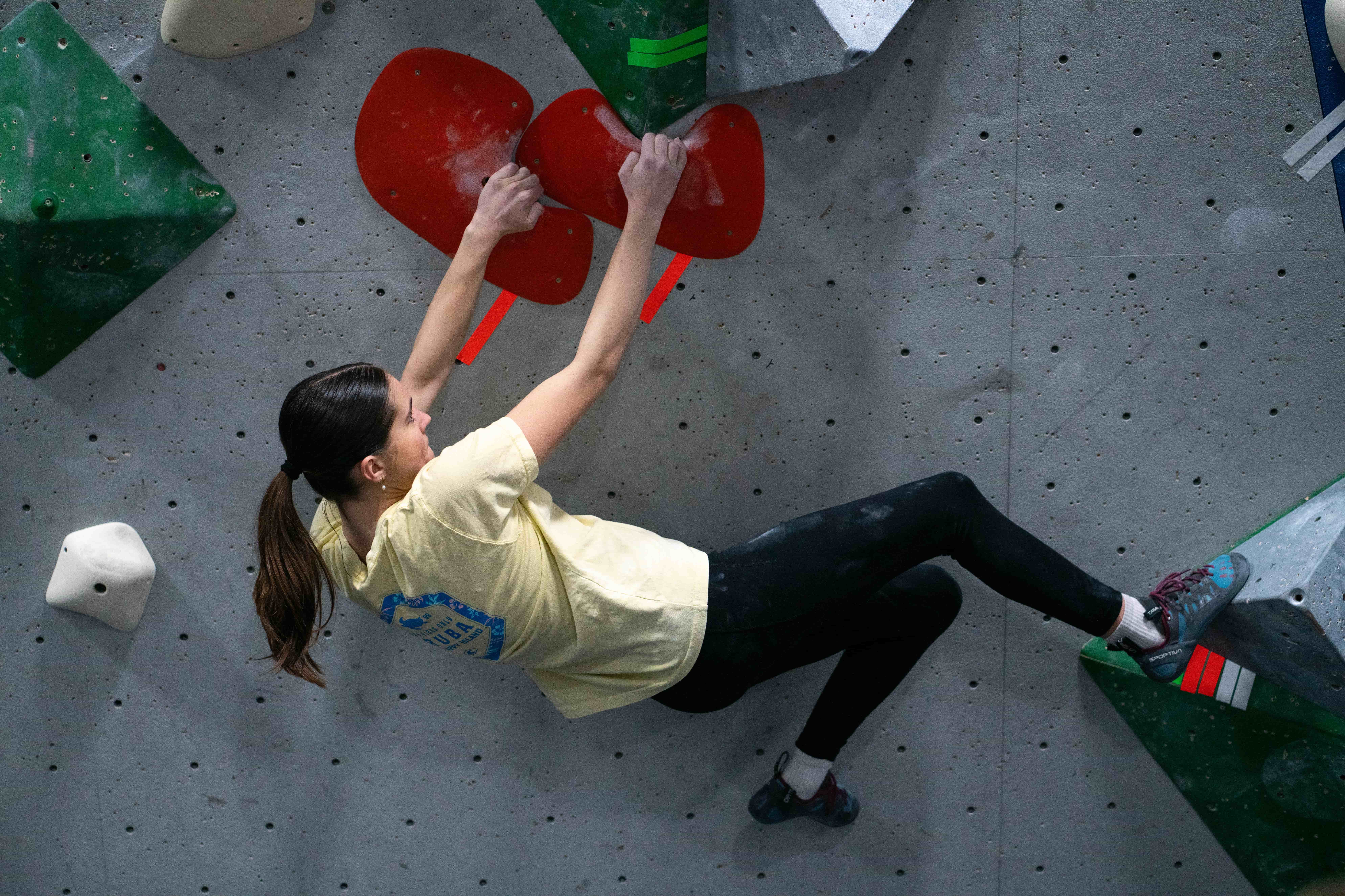 A teenage girl in a yellow shirt climbs an orange boulder