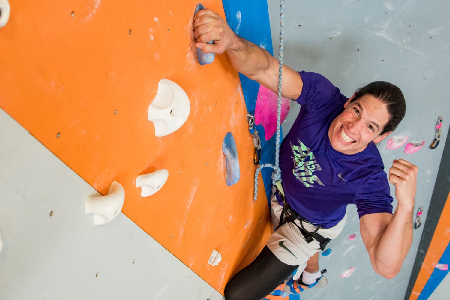 A climber fistpumps and smiling on a climbing wall.