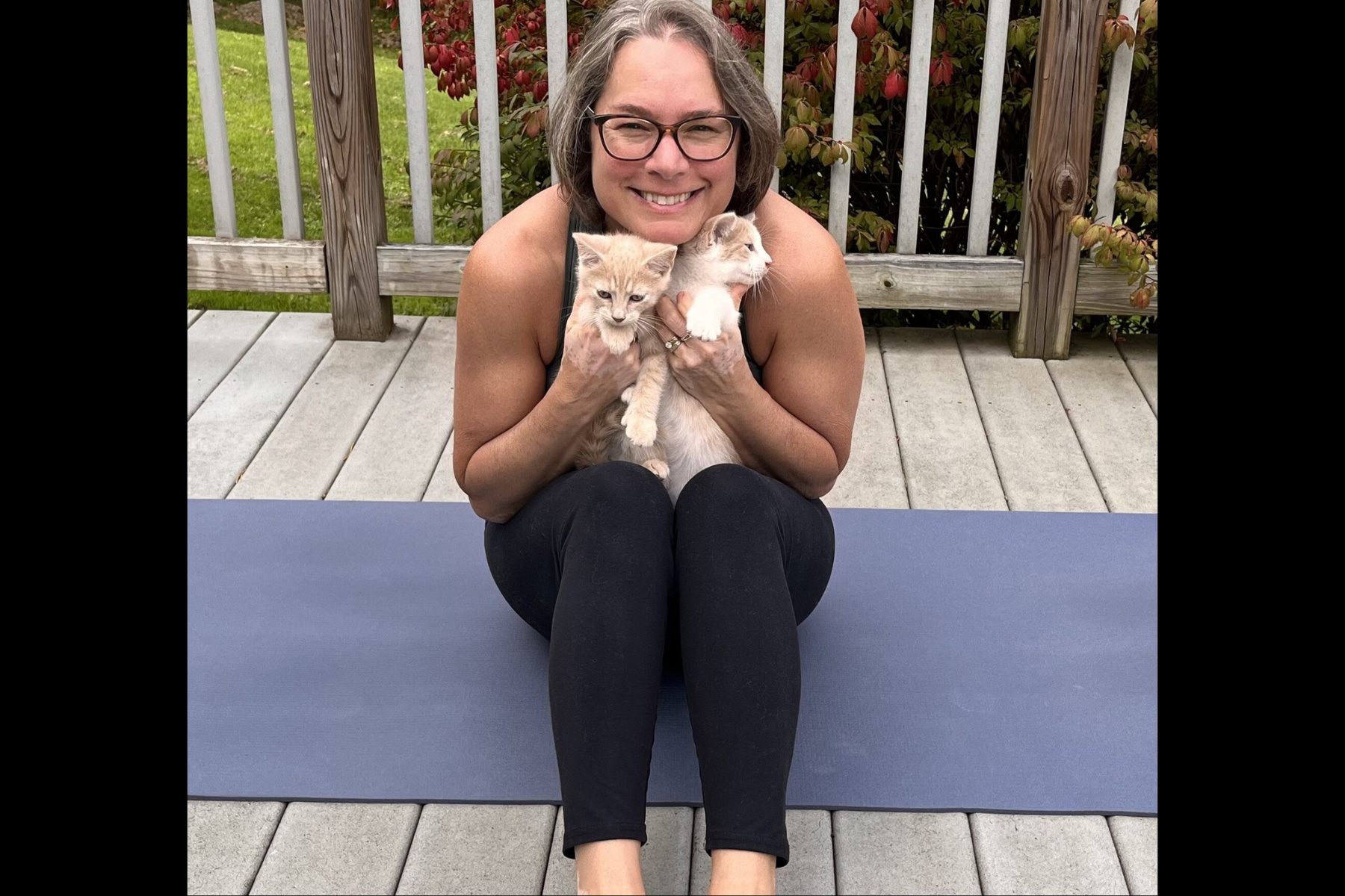 Smiling yoga instructor sitting on her mat with her two kittens.