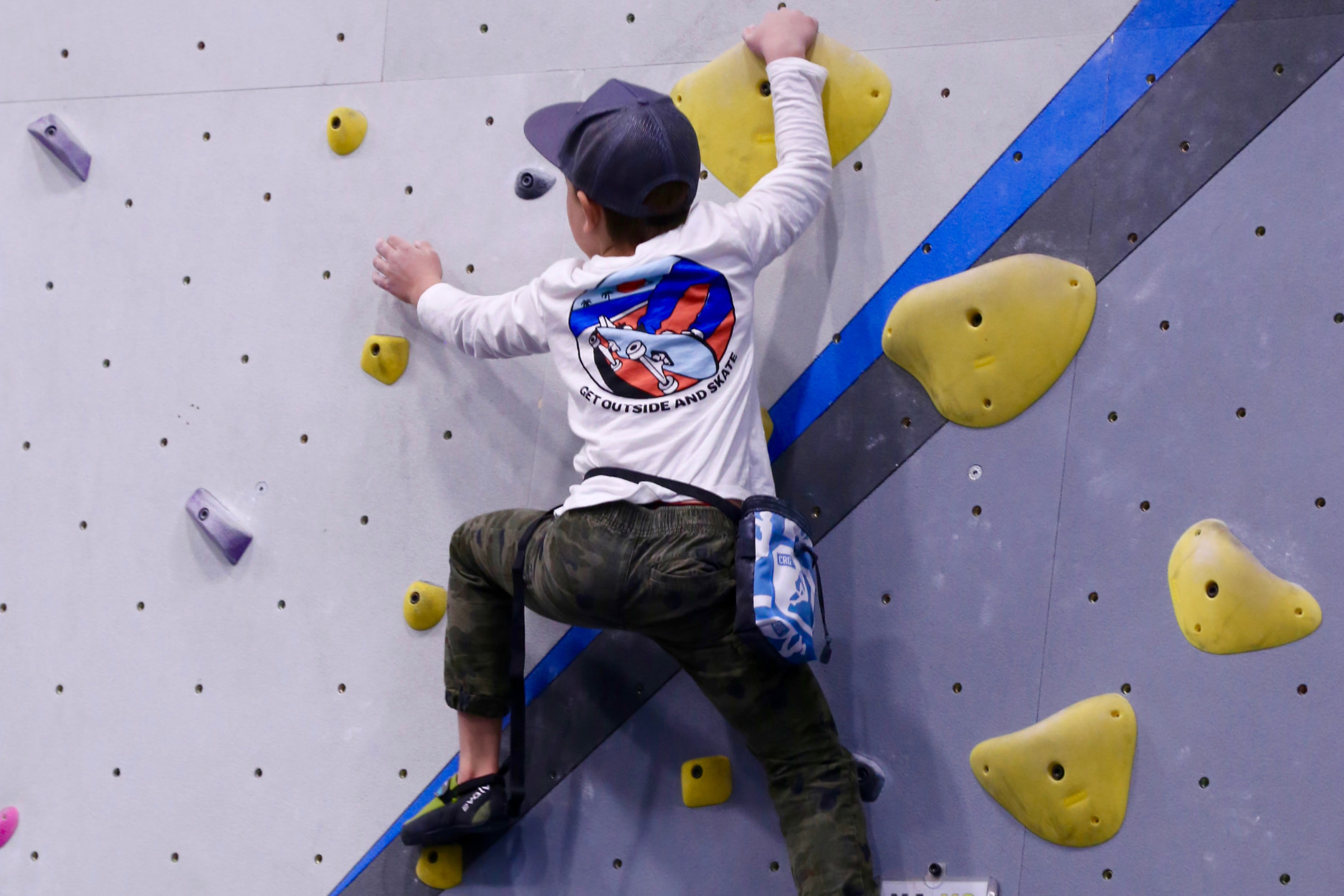 A young boy steps up high on a boulder and gets ready to reach towards the next hold.